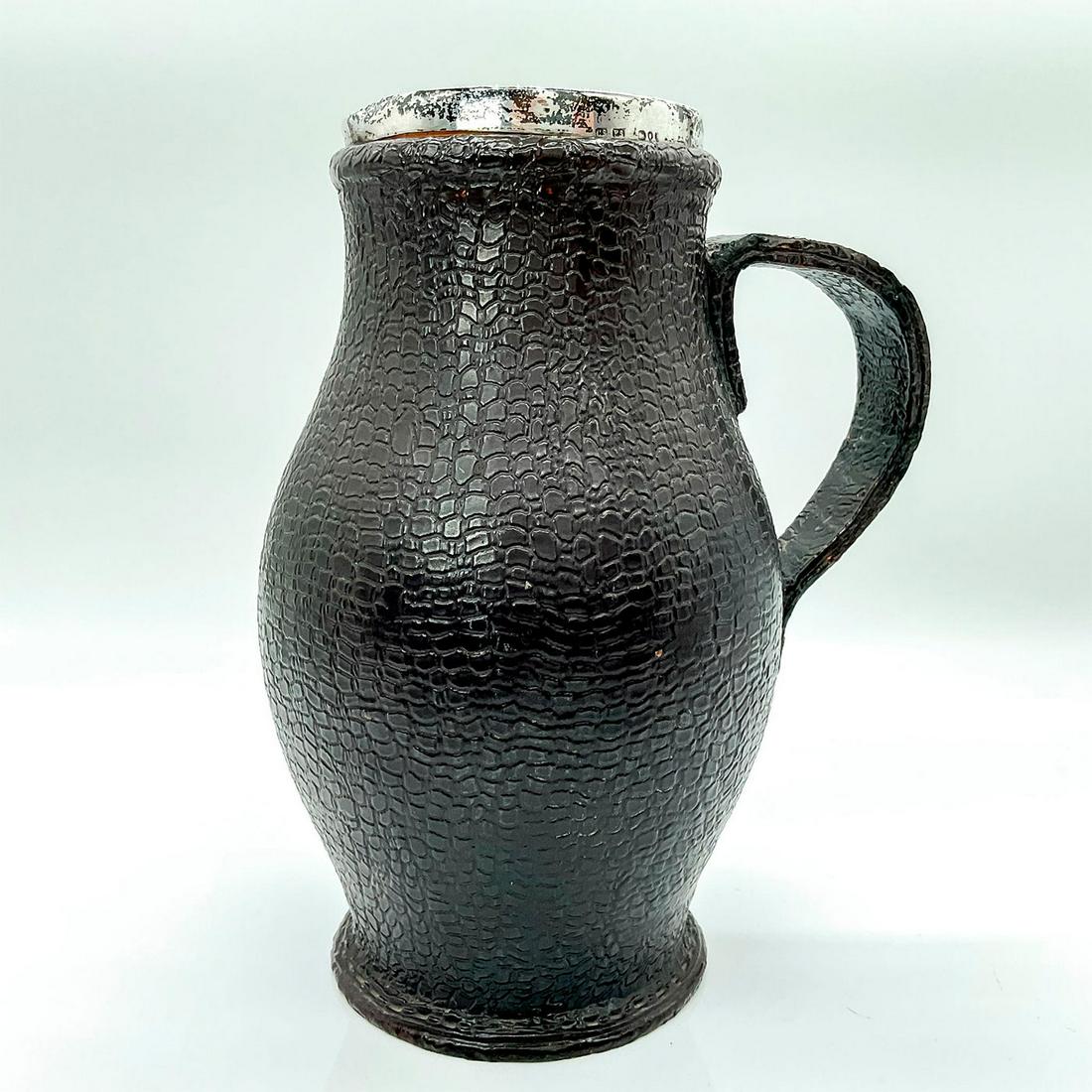 Doulton and Slaters Patent Leatherware, Jug: Rare dark brown leather jug that was made by impressing leather fabric into the surface of clay. Sterling silver rim. Hallmarked â€˜CS PSâ€™ to exterior of rim. Doulton & Slaters Patent impre