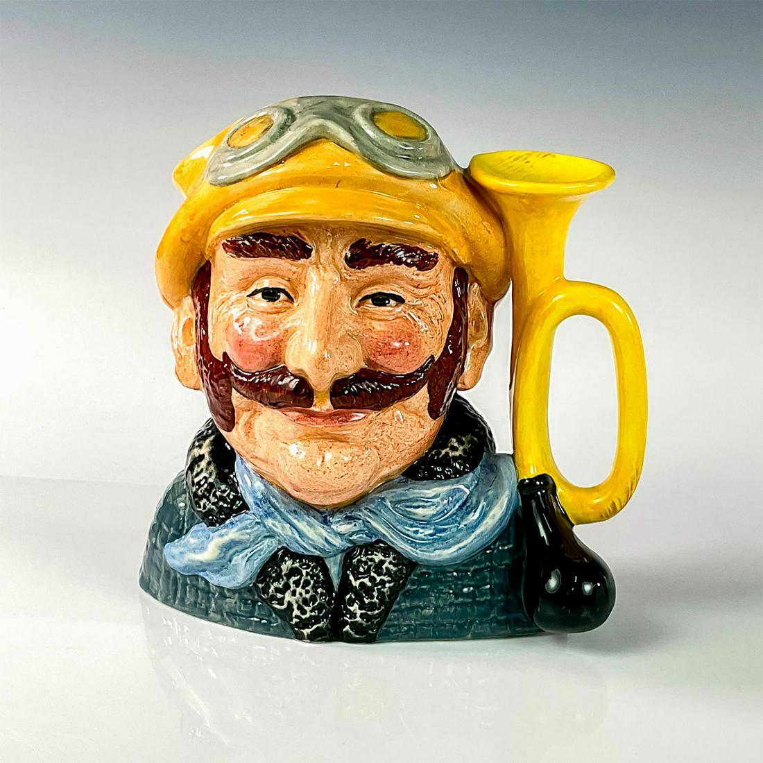 Veteran Motorist D6633 - Large - Royal Doulton Character Jug: Yellow hat, green coat, white scarf. Royal Doulton backstamp. Artist: David B. Biggs Issued: 1973 - 1983 Dimensions: 7.5"H Manufacturer: Royal Doulton Country of Origin: England