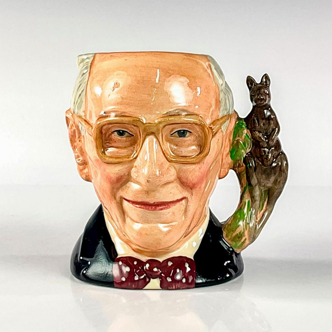 John Shorter D6880 - Small - Royal Doulton Character Jug: Grey hair; black jacket; maroon and white polka-dot. Commissioned by the Characters and Toby Jug Collectors Society of Australia, this depiction of Australian retailer John Shorter was released in 199