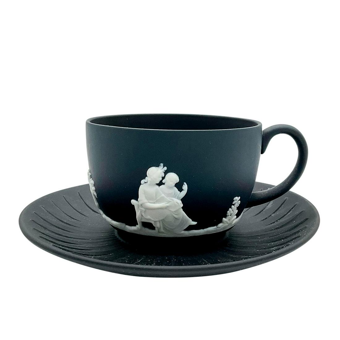 Wedgwood Jasperware Cup and Saucer Set, Boys At Play: Black cup and saucer decorated in a white relief with neoclassical angels at play. Wedgwood impressed to bottom. Saucer measures: 5.75in D. Cup measures: 4.25in W x 2.25in H. Manufacturer: Wedgwood Co