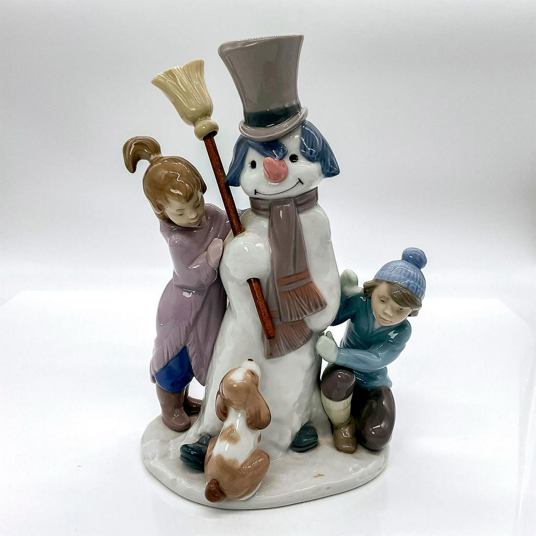 The Snow Man 1005713 - Lladro Porcelain Figurine: Glossy finish porcelain featuring young children building a snowman in the company of their pup. Lladro backstamp. Artist: Francisco Catala Issued: 1990-2019 Dimensions: 5"W x 8.25"H Manufacturer: Lla