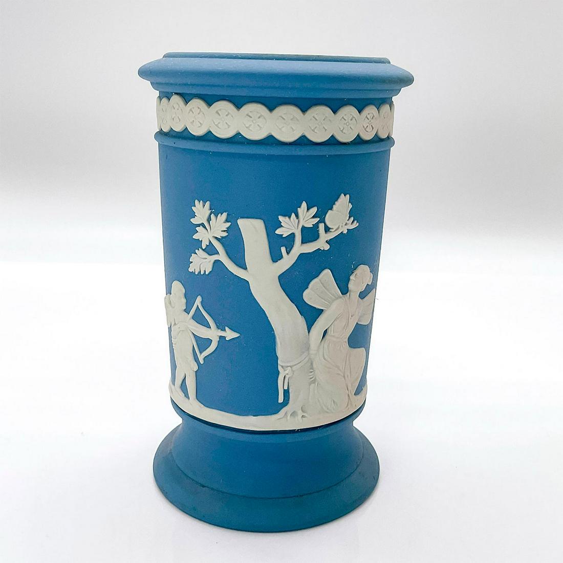 Wedgwood Jasperware Vase, Apollo: Pale blue cylindrical shaped vessel decorated in a white relief with apollo and cupid. Wedgwood Made in England impressed to bottom. Issued: 20th c. Dimensions: 2.75"W x 5"H Manufacturer: Wedgwood Cou