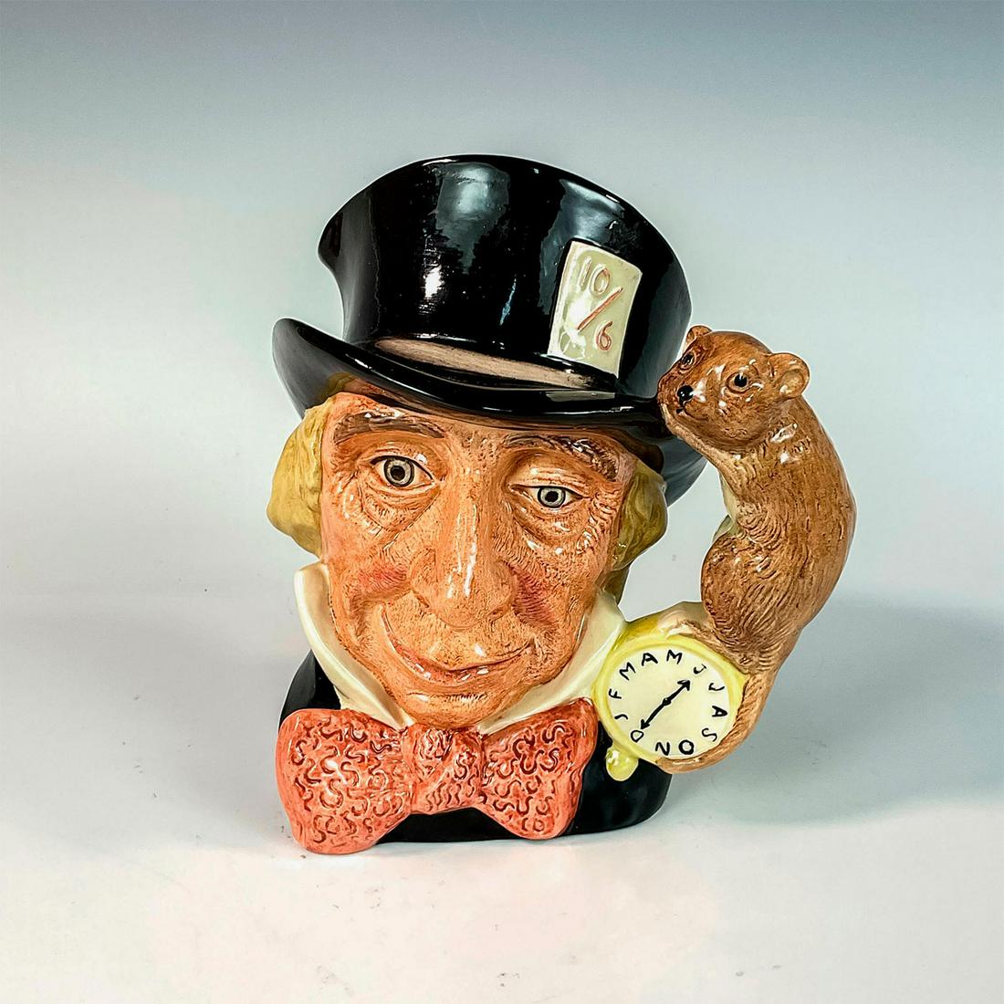 Mad Hatter D6598 - Large - Royal Doulton Character Jug: Variation One. Black hat, dark red bow tie. A character from Lewis Carroll's " Alice's Adventures in Wonderland," the Mad Hatter wears a watch that tells time in months, rather than in hours.Series: A