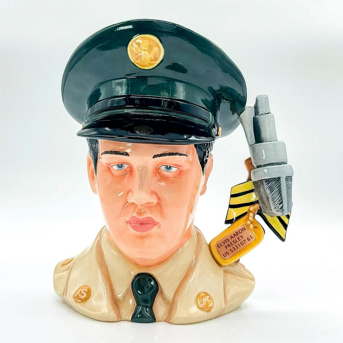 Elvis GI Blues EP9 - Large - Royal Doulton Character Jug: Dog tag, Sergeant stripes, microphone, guitar, and medals handle. G.I. Blues (1960) was Elvis' fifth film. The soundtrack album became the top-selling album of his career. Handle represents his tw