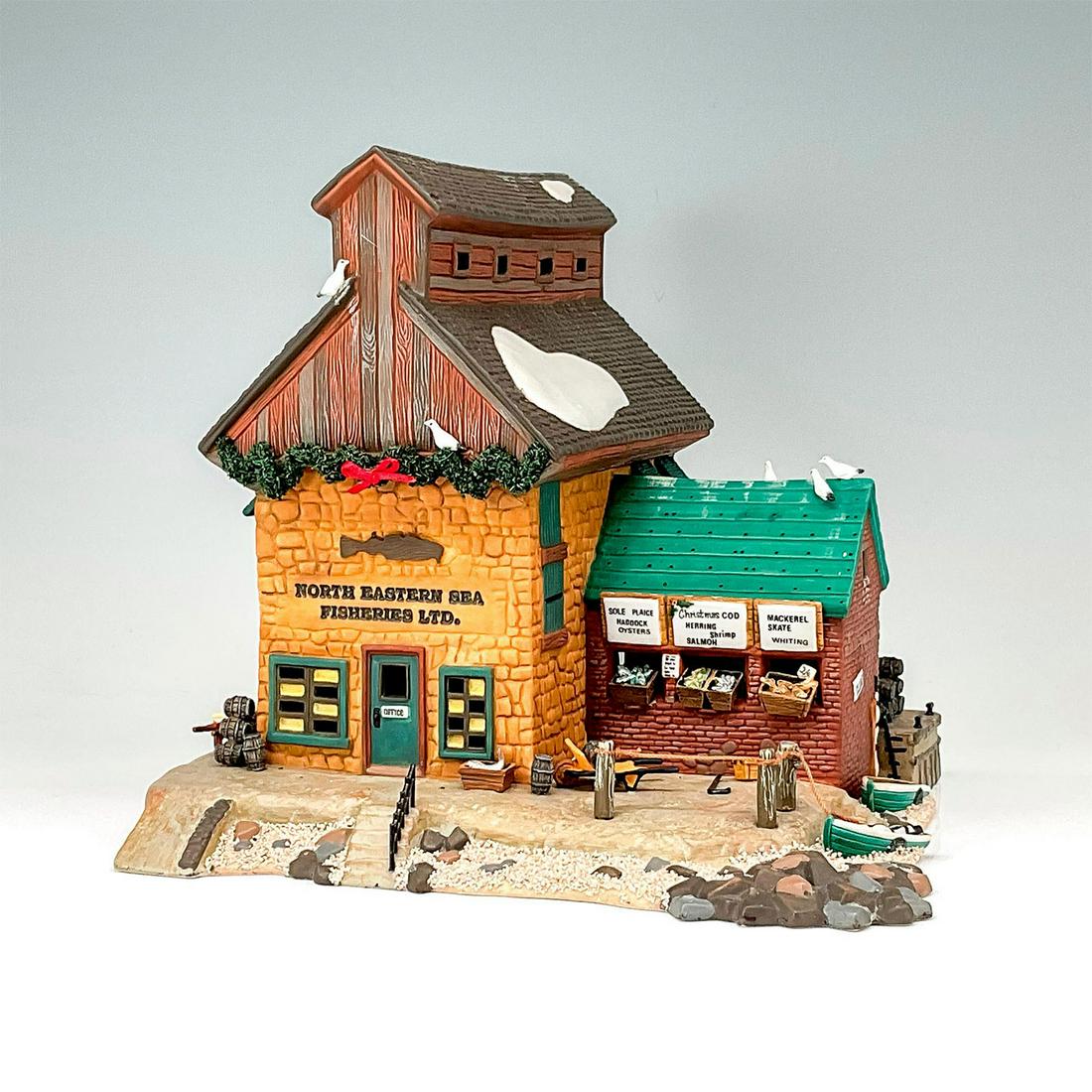 Department 56 Figure, North Eastern Fisheries LTD: Part of the Dickens' Village Series. Hand-painted porcelain figure modeled as a Christmas decorated cobblestone building with fish market and boats lining the shore outside. Light switch cord included