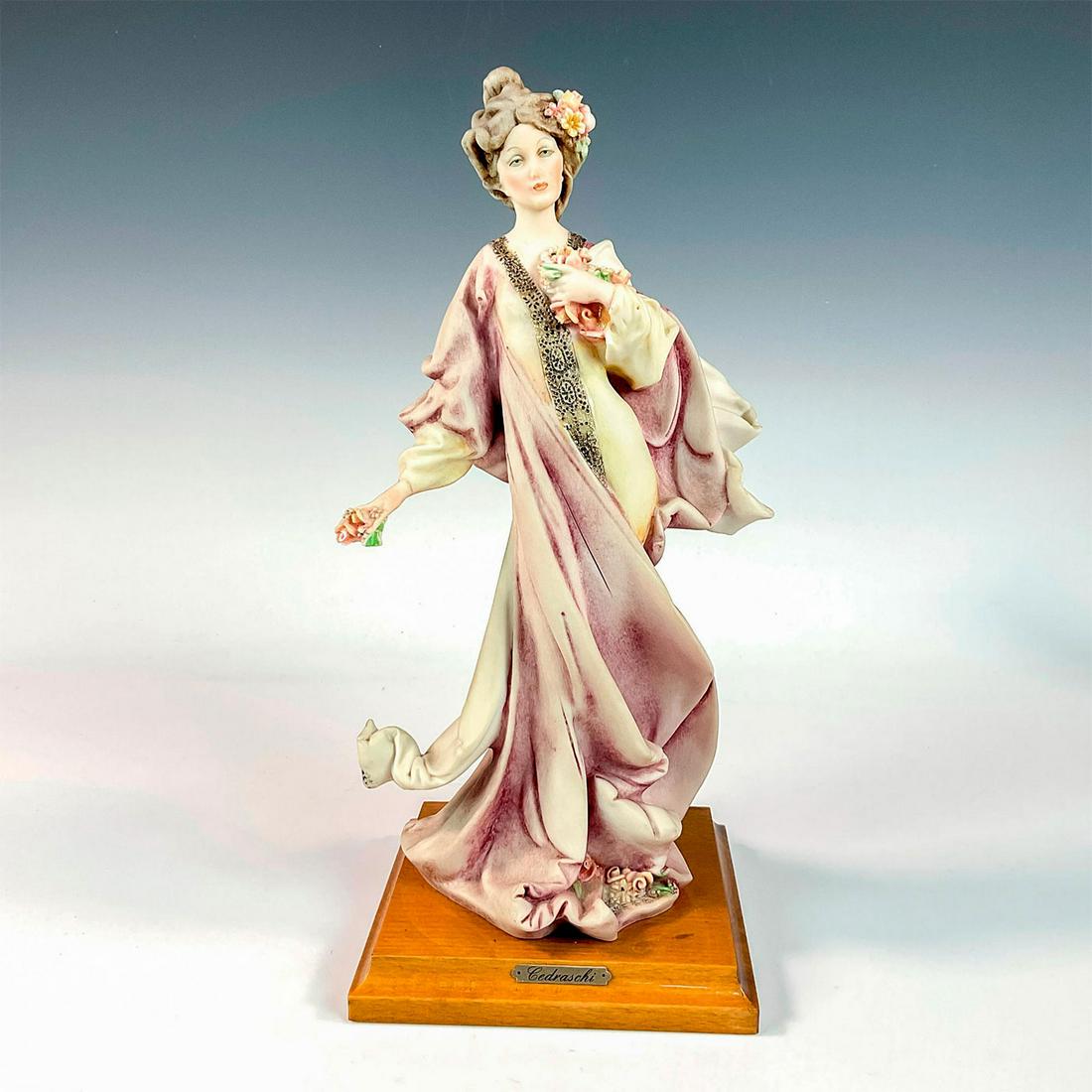 Capodimonte P. Cedraschi Figurine, Woman with Flowers: Vintage Capodimonte figurine modeled as Italian woman wearing a flowing pink dress holding a bouquet of flowers. Fixed to wood base. Capodimonte backstamp. Cedraschi inscribed to dress. Artist: P. Ced