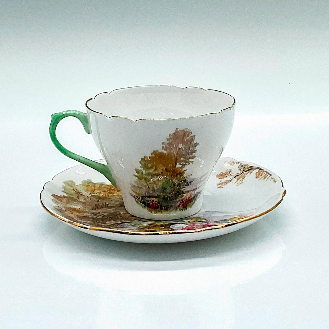 Shelley Fine Bone China Cup and Saucer, Heather: A white ground teacup set depicting a rural English scene, and accented by gold trims. Shelley backstamps. Teacup: 3.75"L x 3"W x 2.25"H. Saucer: 0.75"H x 5"dia. Issued: c. 1932 Manufacturer: Shelley