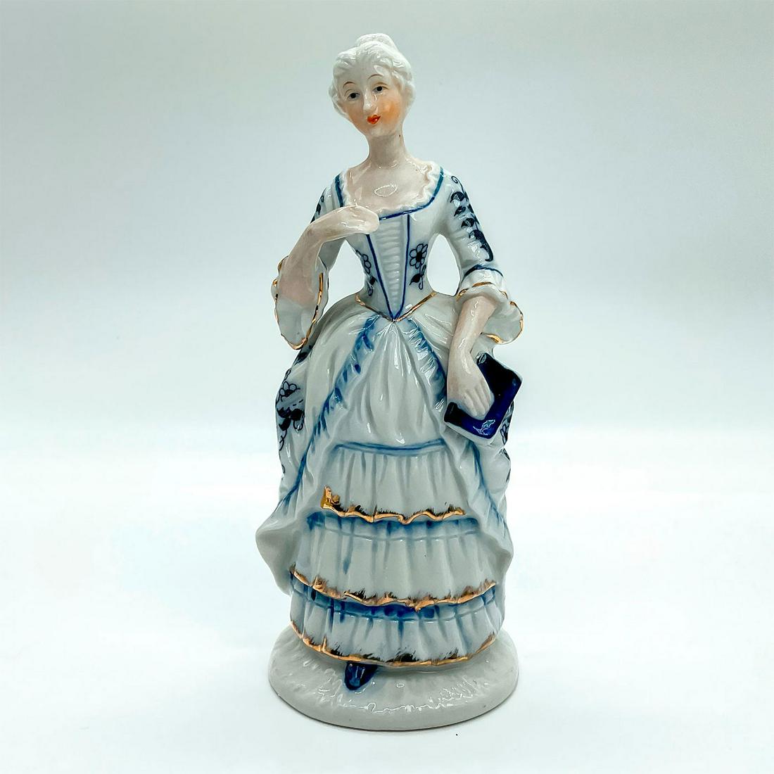 Vintage Porcelain Figurine, Lady With Book: Hand painted figure of lady in a blue and white layered dress with gold guilt, holding a blue book. Made in Taiwan label on base. This item has no reserve. Dimensions: 7.5"H