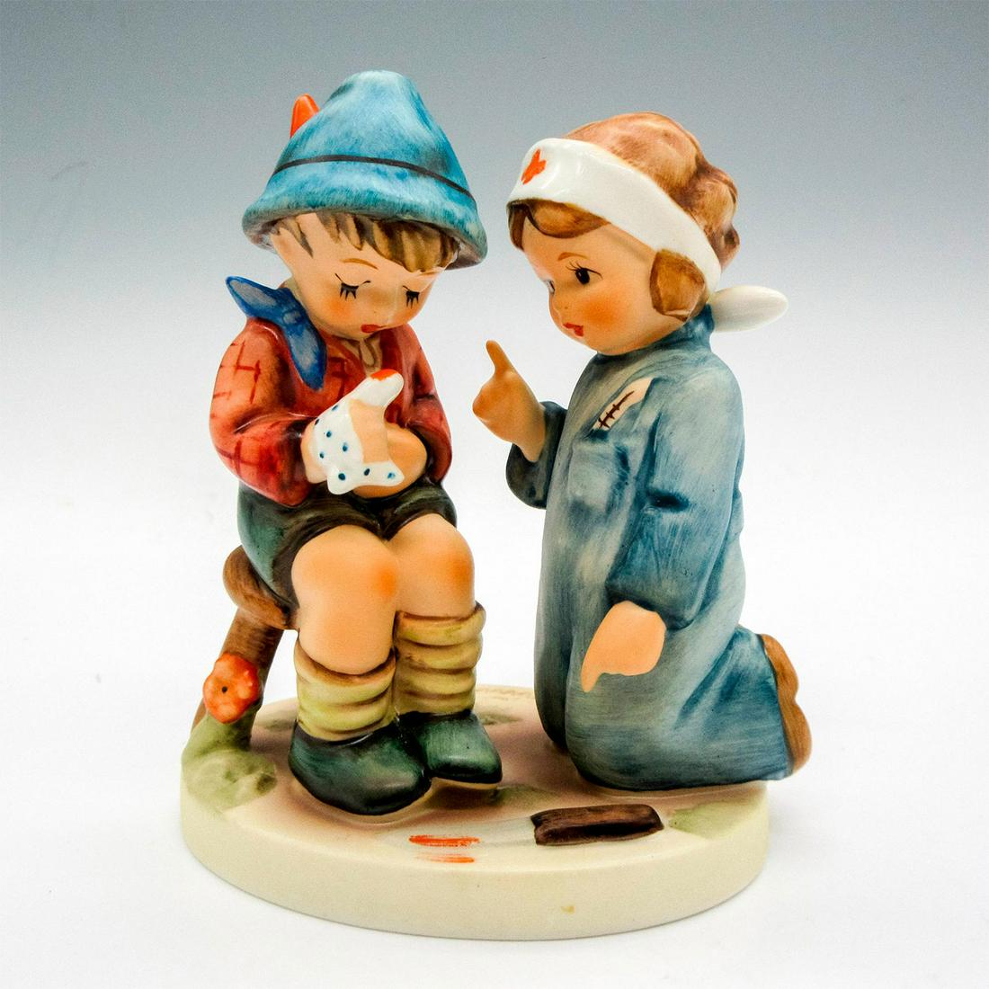 Goebel Hummel Figurine Little Nurse: Figurine of a young doctor making a house call to an injured friend. Matte finish collectable on round base. "Little Nurse: Hansel, merk dir das" sticker on the back. Goebel backstamp. Artist: M.I. Hu