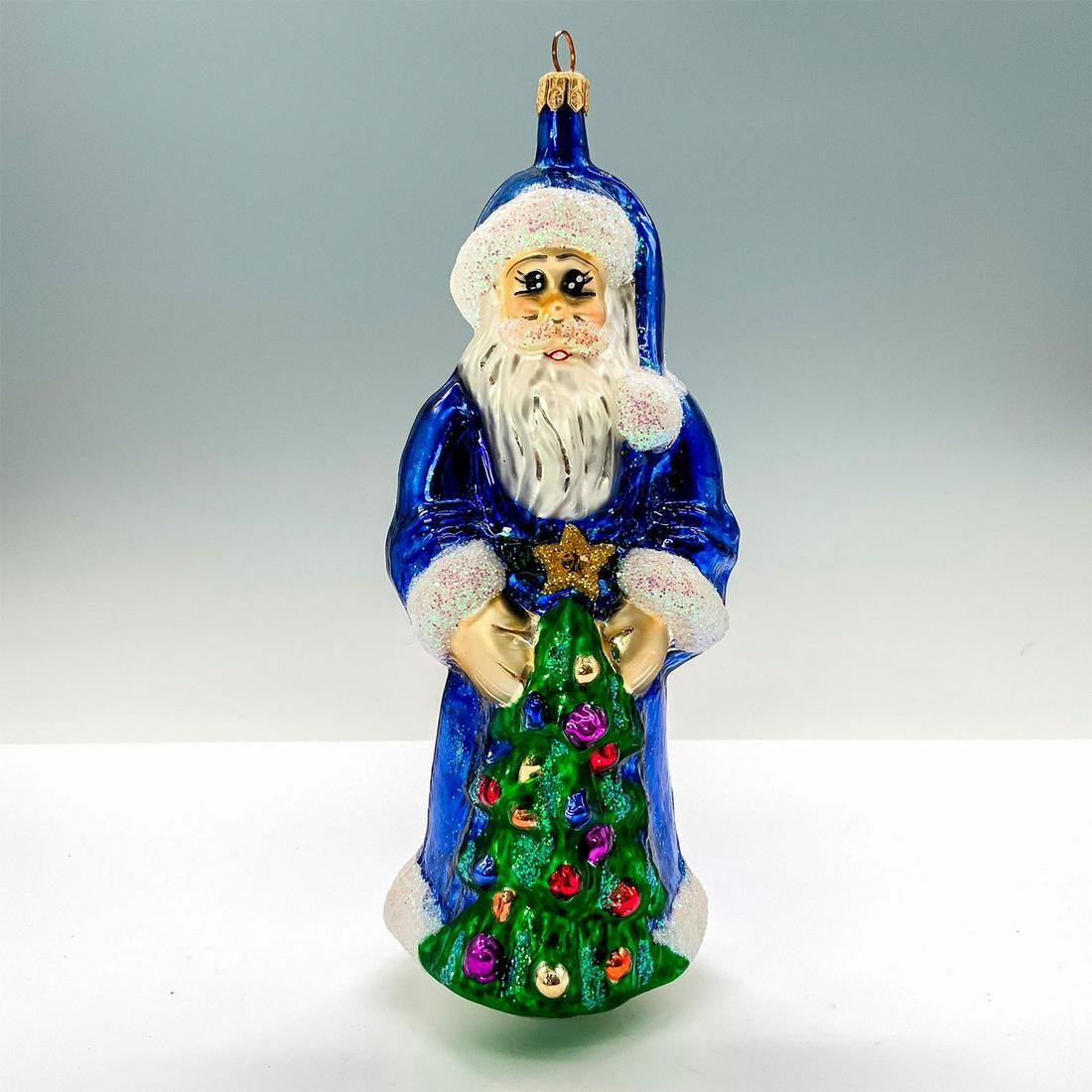 Christopher Radko Christmas Ornament, European Santa Clause: A Christmas ornament of Santa Clause dressed in blue holding a petite decorated Christmas tree. The ornament is decorated with glitter throughout. Dimensions: 3"L x 3"W x 7.5"H Manufacturer: Christoph