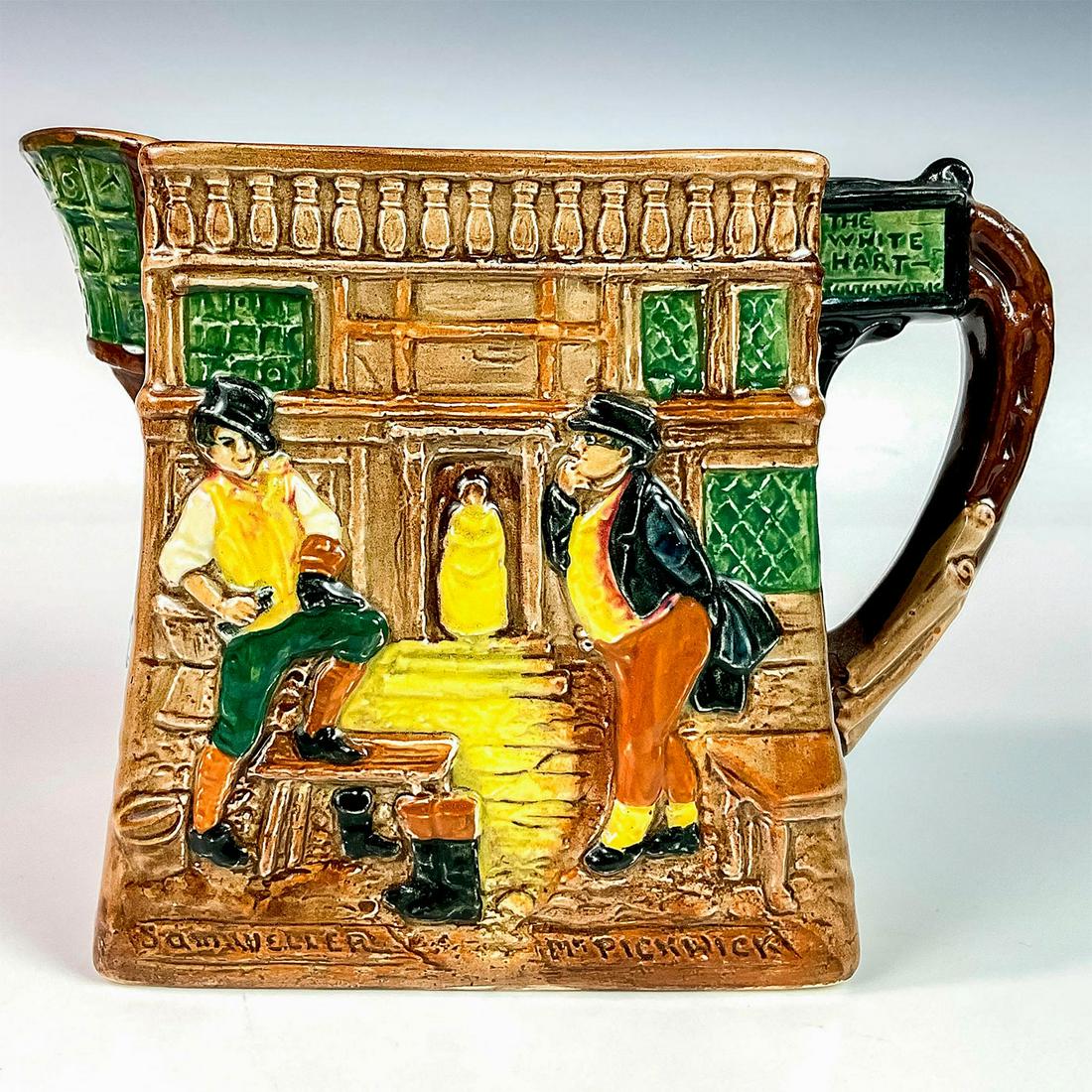 Royal Doulton Dickens Ware Pitcher, The Pickwick Papers: Glazed porcelain pitcher embossed with various characters from the novel The Pickwick Papers. Royal Doulton backstamp. Issued: 1902-1956 Dimensions: 7.5”L x 4.25”W x 5.5”H Manufactur