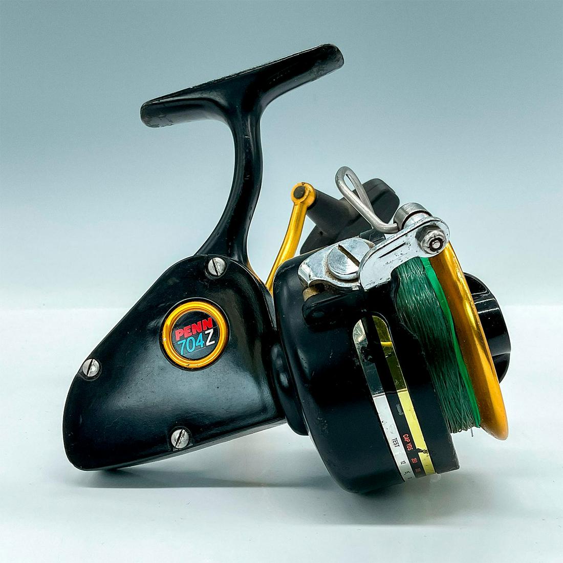 Vintage Penn 704Z Spinning Reel: Second generation of the 700 Series. Nice looking black base with gold handle and spool, line cap for 12 lbs. is 350 yds. Issued: 20th Century Dimensions: 6"L x 5.75"W x 4"H Manufacturer: Penn Country