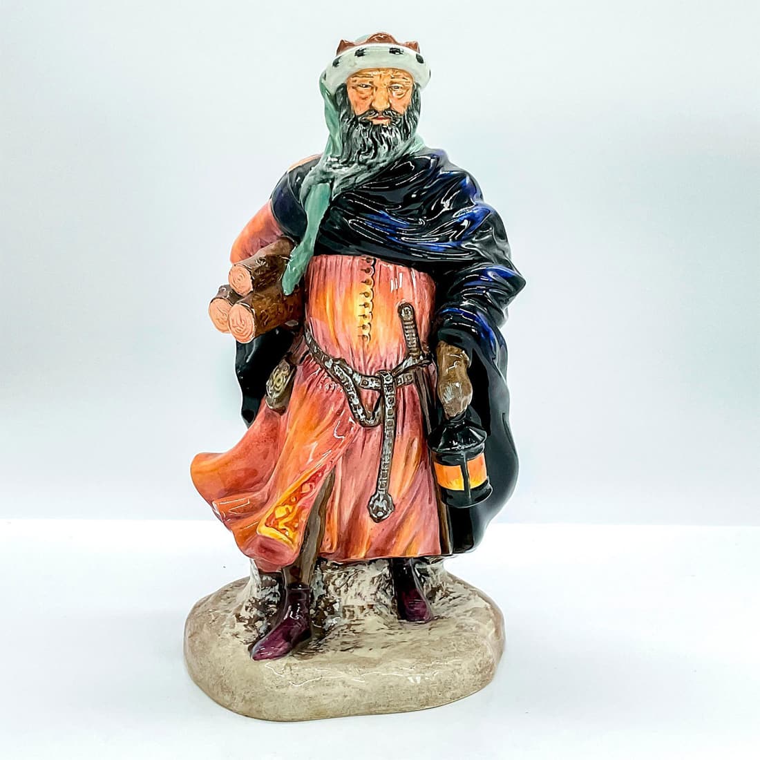 Good King Wencelas HN3262 - Royal Doulton Figurine: Pink-orange tunic, black and purple wrap; holding a lantern and bundle of firewood. Royal Doulton backstamp. Issued: 20th c. Dimensions: 4.75"L x 4.25"W x 9"H Manufacturer: Royal Doulton Country of Or