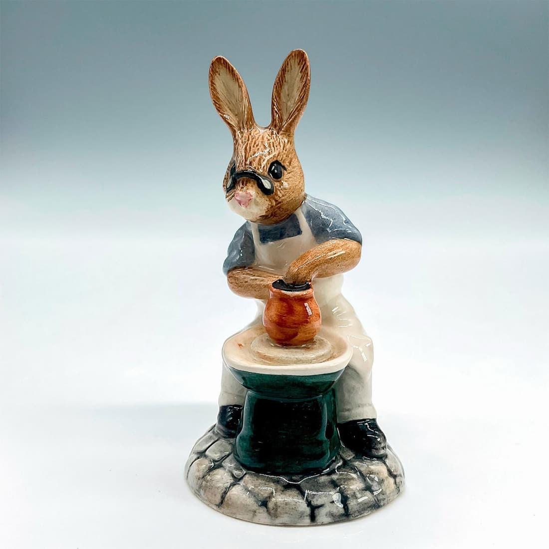 Master Potter DB131 - Royal Doulton Bunnykins: Royal Doulton Bunnykins, Master Potter Bunnykins DB131 (blue white, green and brown). Royal Doulton backstamp. Artist: G. Tongue Issued: 1992 - 1993 Dimensions: 2.25"L x 2"W x 3.75"H Manufacturer: Roy