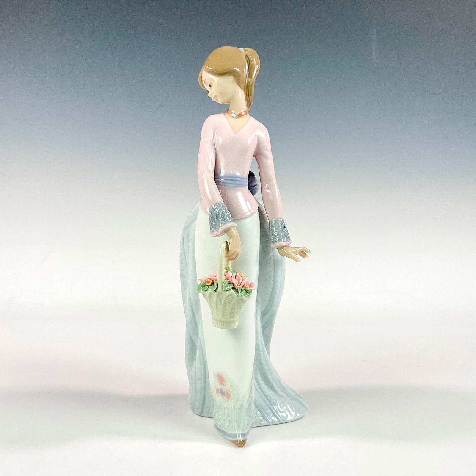 Basket Of Love 1007622 - Lladro Porcelain Figurine: Glossy finish; Lladro backstamp. Artist: Jose Puche Issued: 1994 - 1994 Dimensions: 9.75"H x 4"W Manufacturer: Lladro Country of Origin: Spain