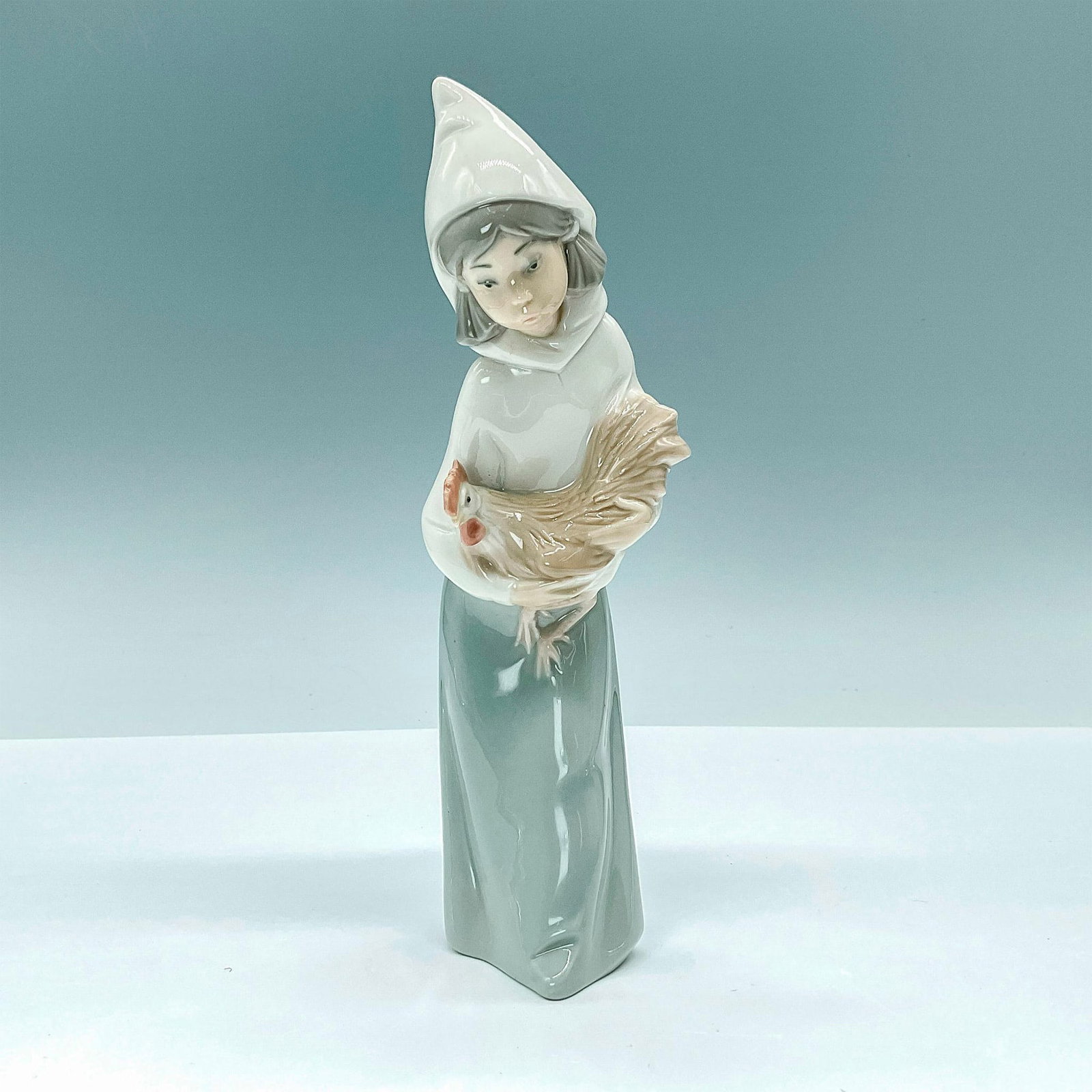 Girl with Rooster 1004677 - Lladro Porcelain Figurine: This beautiful, glazed figure depicts a young, hooded girl carrying a highly detailed rooster. Lladro backstamp. Artist: Juan Huerta Issued: 1969-2001 Dimensions: 3"L x 2.75"W x 7.75"H Manufacturer: L