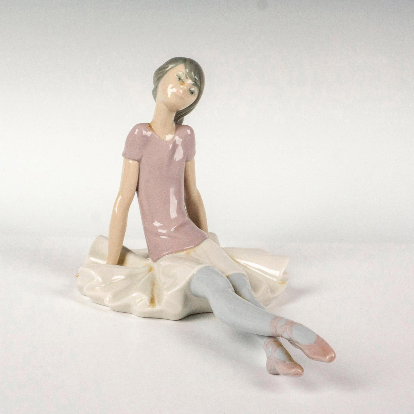 Phyllis 1001356 - Lladro Porcelain Figurine: Glossy finish modeled as a young girl seated. Lladro backstamp. Artist: Juan Huerta Issued: 1978-1993 Dimensions: 5"L x 9.25"W x 6.25"H Manufacturer: Lladro Country of Origin: Spain