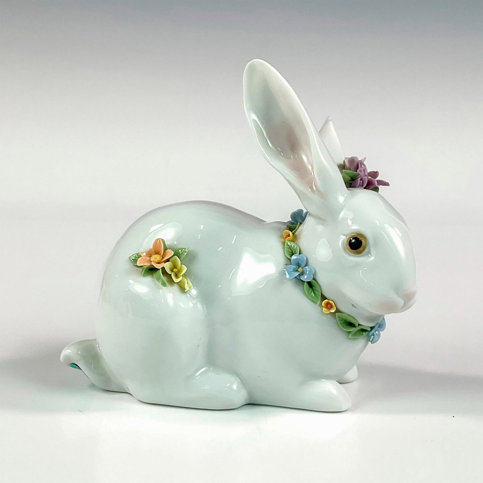 Attentive Bunny With Flowers 1006098 - Lladro Porcelain Figurine: Glossy finish; Lladro backstamp. Includes original box. Box measures: 8"L x 5.25"W x 5"H. Artist: Juan Huerta Issued: 1994 Dimensions: 4.5"H x 4.75"W Manufacturer: Lladro Country of Origin: Spain<