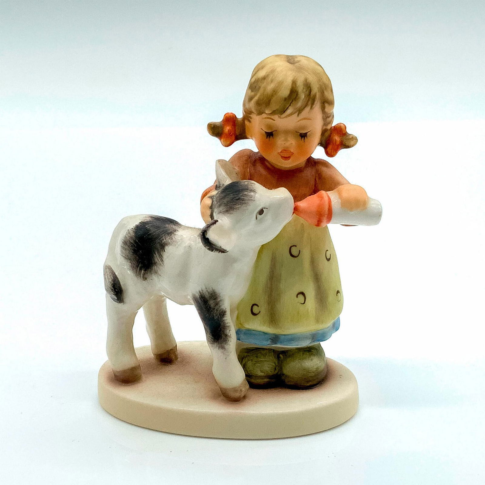 Goebel Hummel Figurine, Friendly Feeding: Hummel Figurine #2231; Matte porcelain, hand painted. Young girl feeding a calf. 'M. I. Hummel' inscribed on back of base. Goebel backstamp on bottom. Issued: 2005-2008 Dimensions: 2.5"L x 1.5"W x 3.2