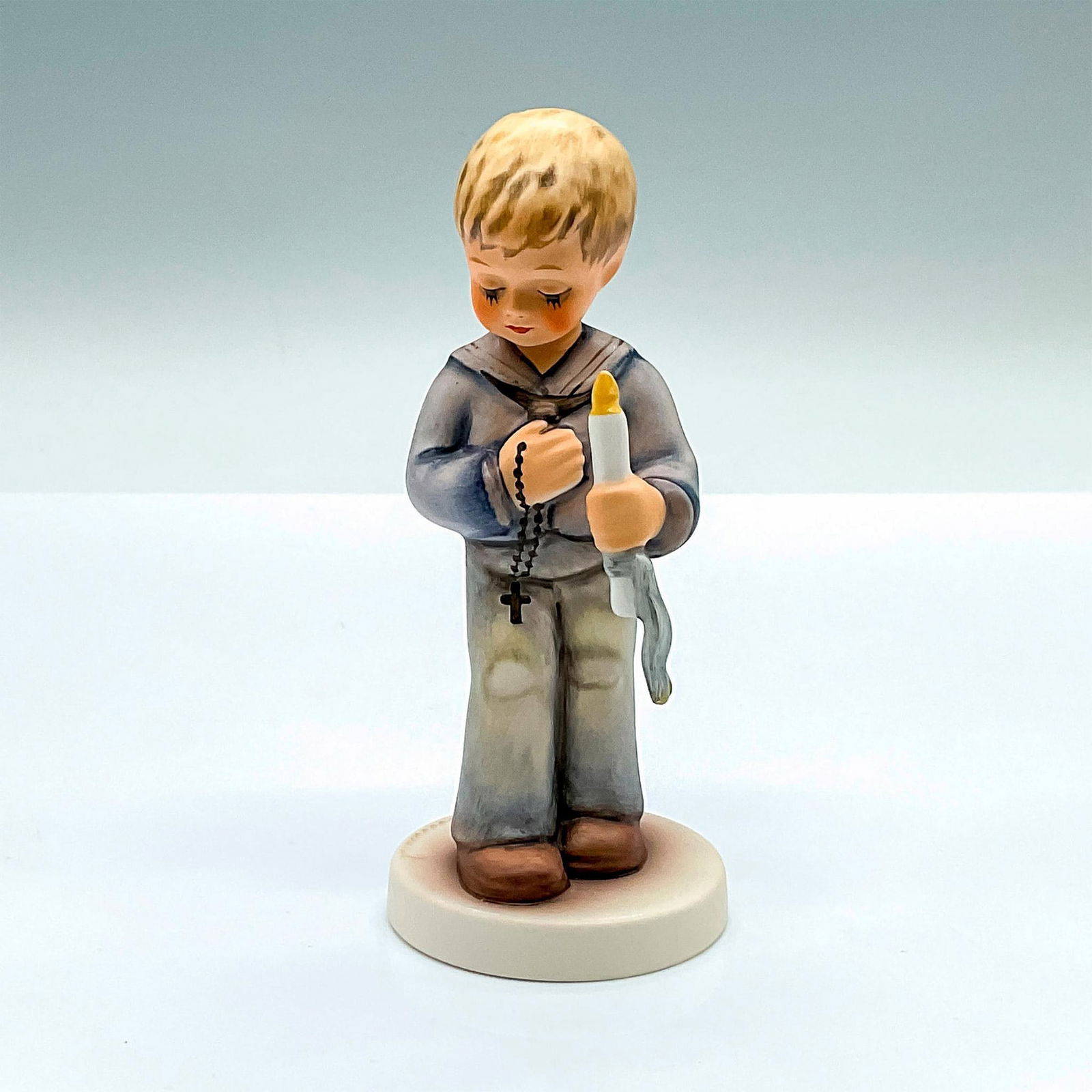 Goebel Hummel Figurine, Heavenly Prayer: Hand painted figure of a young boy holding a candle and rosary beads. Goebel Hummel backstamp. Issued: c. 1990-1999 Dimensions: 2.25"L x 2"W x 4.75"H Manufacturer: Goebel Hummel Country of Origin: Ger