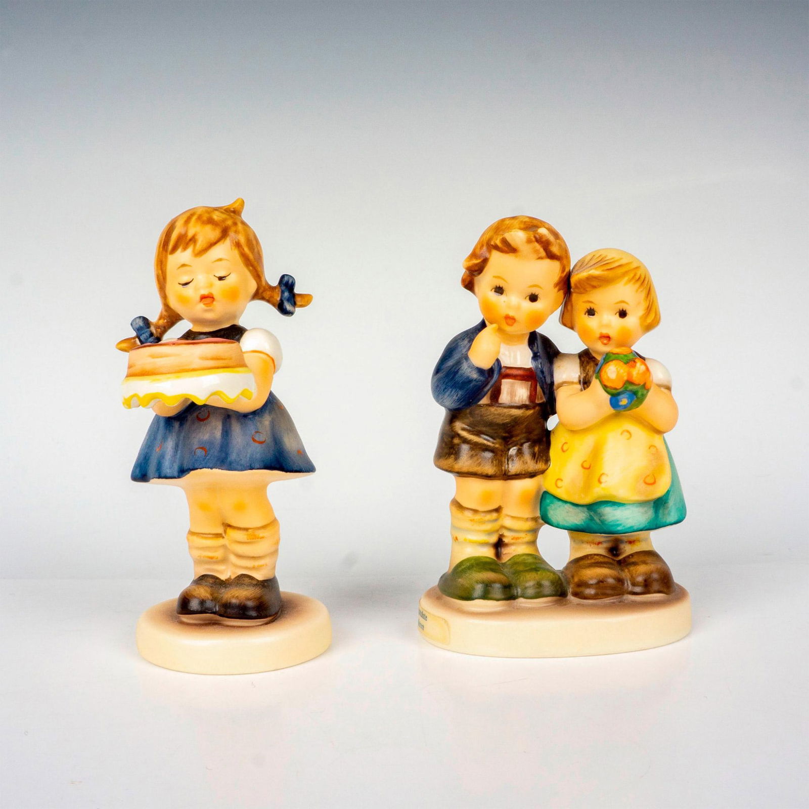 2pc Goebel Hummel Figurines: Hand painted in matte finish titled We Congratulate and Sweet As Can Be. M. I. Hummel impressed backstamp. Goebel backstamp. Largest measures: 2.5"L x 1.75"W x 4"H. Shortest measures: 1.75"W x 4.25"H.