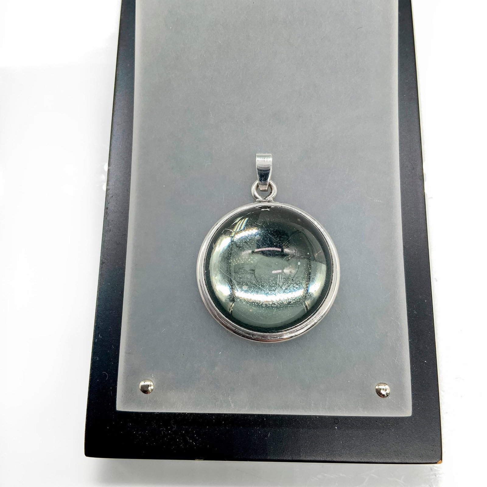 Lalique Sterling Silver Smokey Grey Cabochon Crystal Pendant: Sterling silver pendant with a grey crystal cabochon. Dimensions: 1" dia. Manufacturer: Lalique Country of Origin: France Provenance: Collection of Marie-Claude Lalique