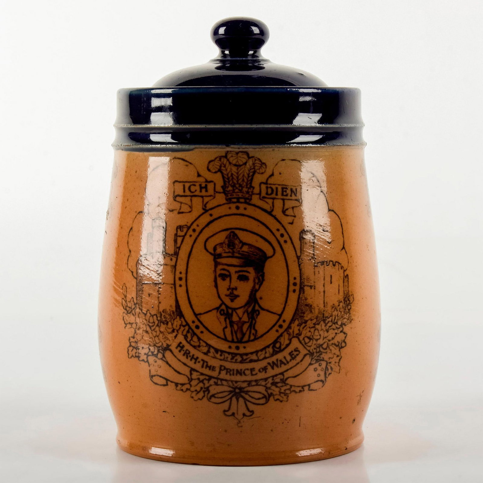 Doulton Lambeth Commemorative Tobacco Jar, King Edward VIII: Investiture of the Prince of Wales 1911. Features printed portrait of the Prince and view of Caernarvon Castle. Stoneware; blue glazed rim and lid. Doulton backstamp. Crazing to lid; lid sealed. Weigh
