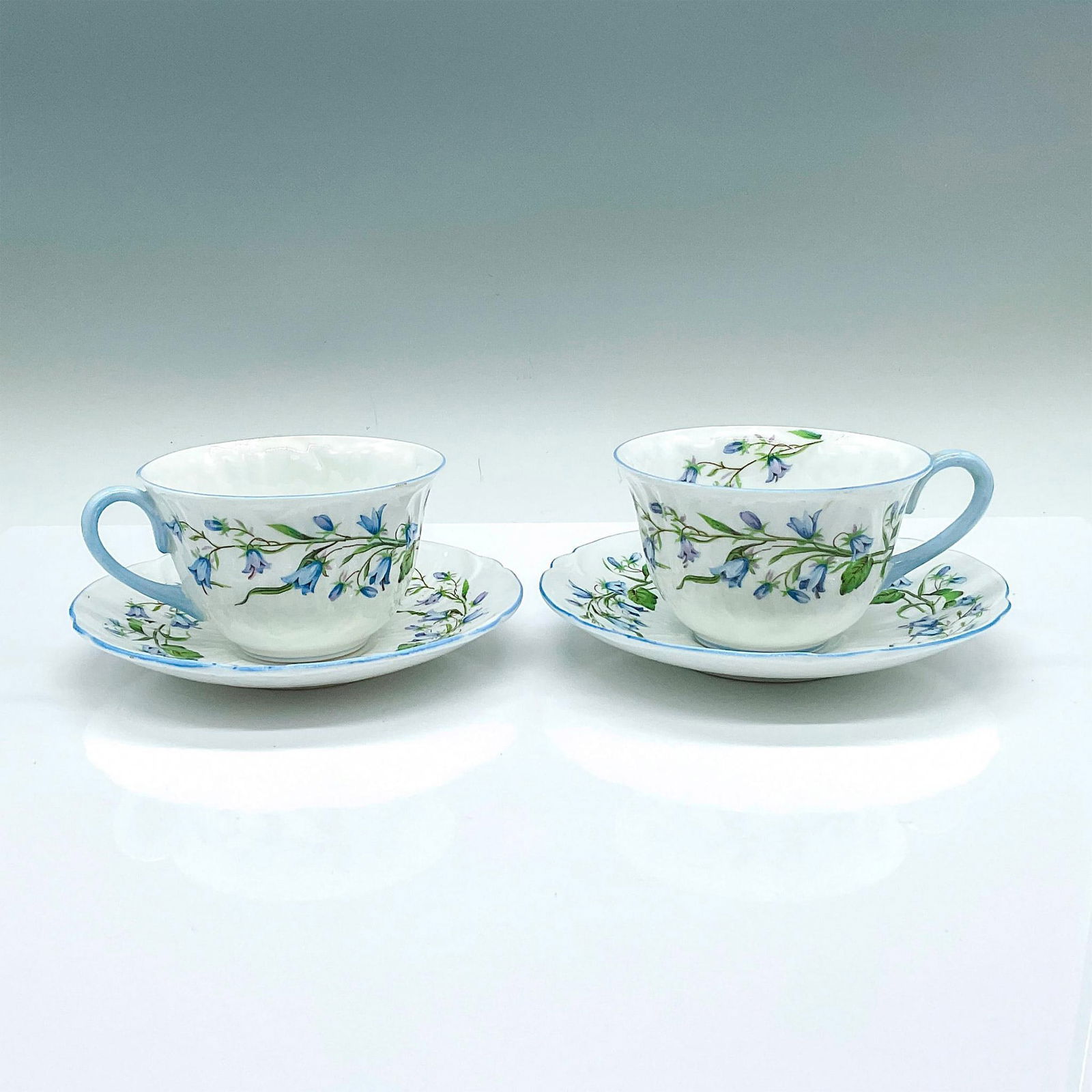 4pc Shelley Bone China Tea Cups and Saucers, Harebell: 2 cups with matching 2 saucers, adorned with blue flower pattern and light blue trims. Shelley backstamps. Cup: 4.5"L x 3.75"W x 2.25"H. Saucer: 5.75"W x 1"H. Pattern number: 13590. Issued: 20th centu