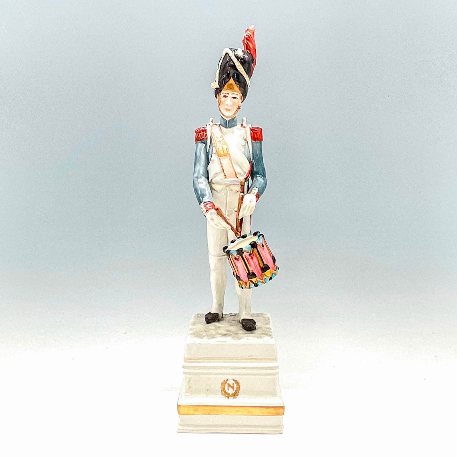 Cacciapuoti Porcelain Napoleonic Figurine, Tambour: A Guido Cacciapuoti figurine depicting Napoleonic era imperial French soldier on a raised porcelain pedestal with gilt N within a wreathed medallion to front, and name of piece inscribed to verso of p