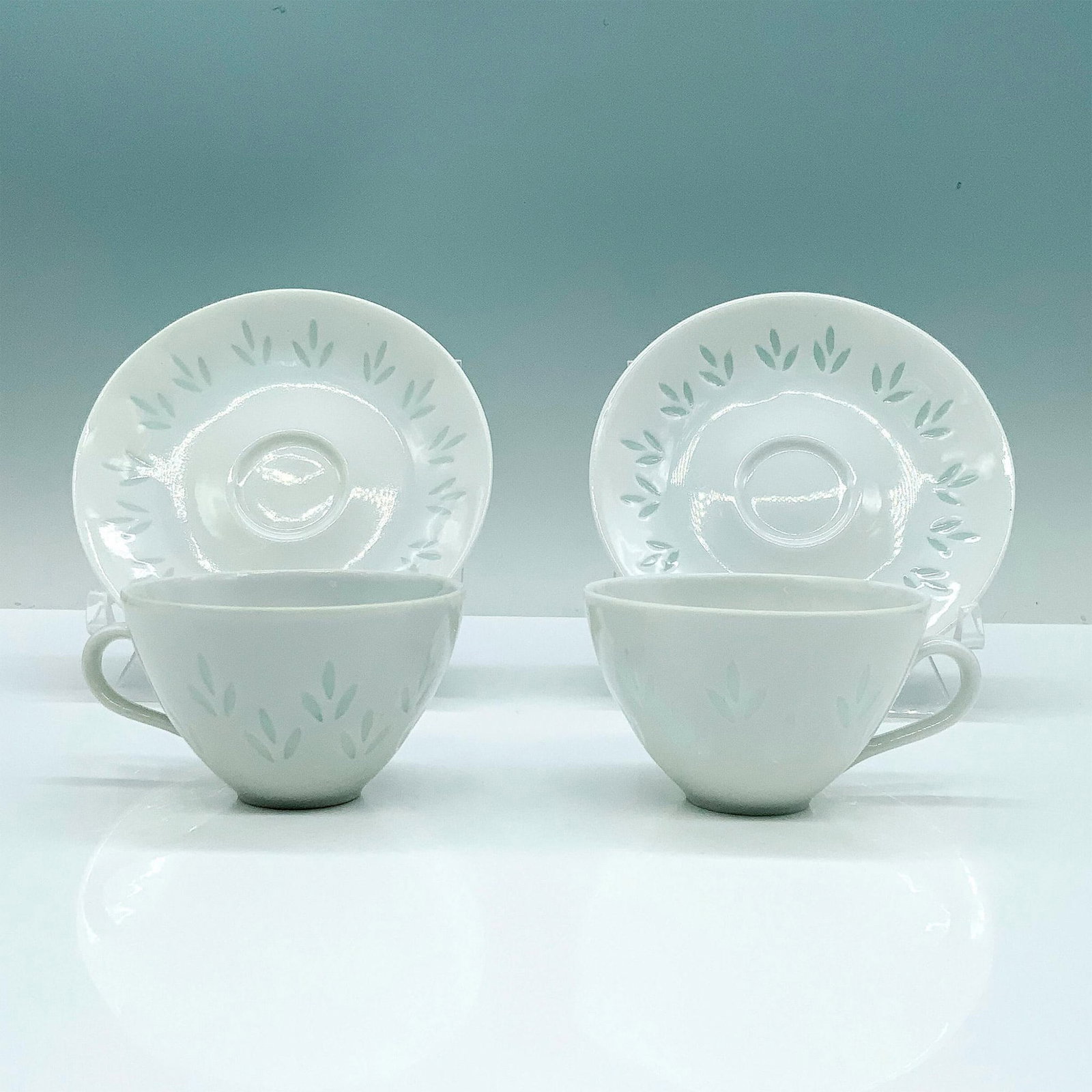 4pc Arabia Finland Lehti Teacups and Saucers Set: A set of 2 white teacups and 2 white saucers decorated with opaque foliage designs throughout the items. Arabia Finland backstamp. Dimensions of the teacups: 3.5"L x 2.5"W x 2"H. Dimensions of the sau