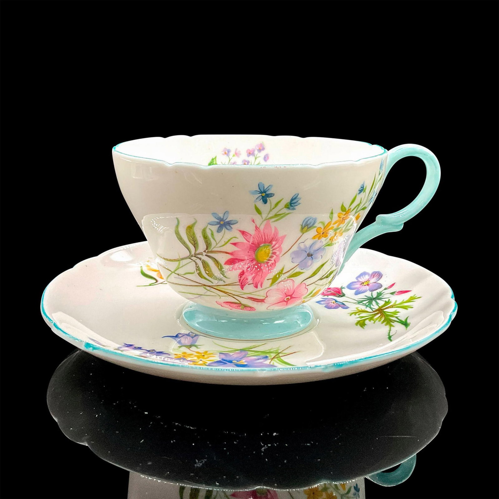 2pc Shelley England Cup and Saucer, Wild Flowers: Vintage white bone china with dainty colorful flowers, blue rims. Henley shape. Tea cup 4"L x 3.5"W x 2.5"H. Saucer 0.75"H x 5.5"dia. Shelley England backstamp. Manufacturer: Shelley Country of Origin