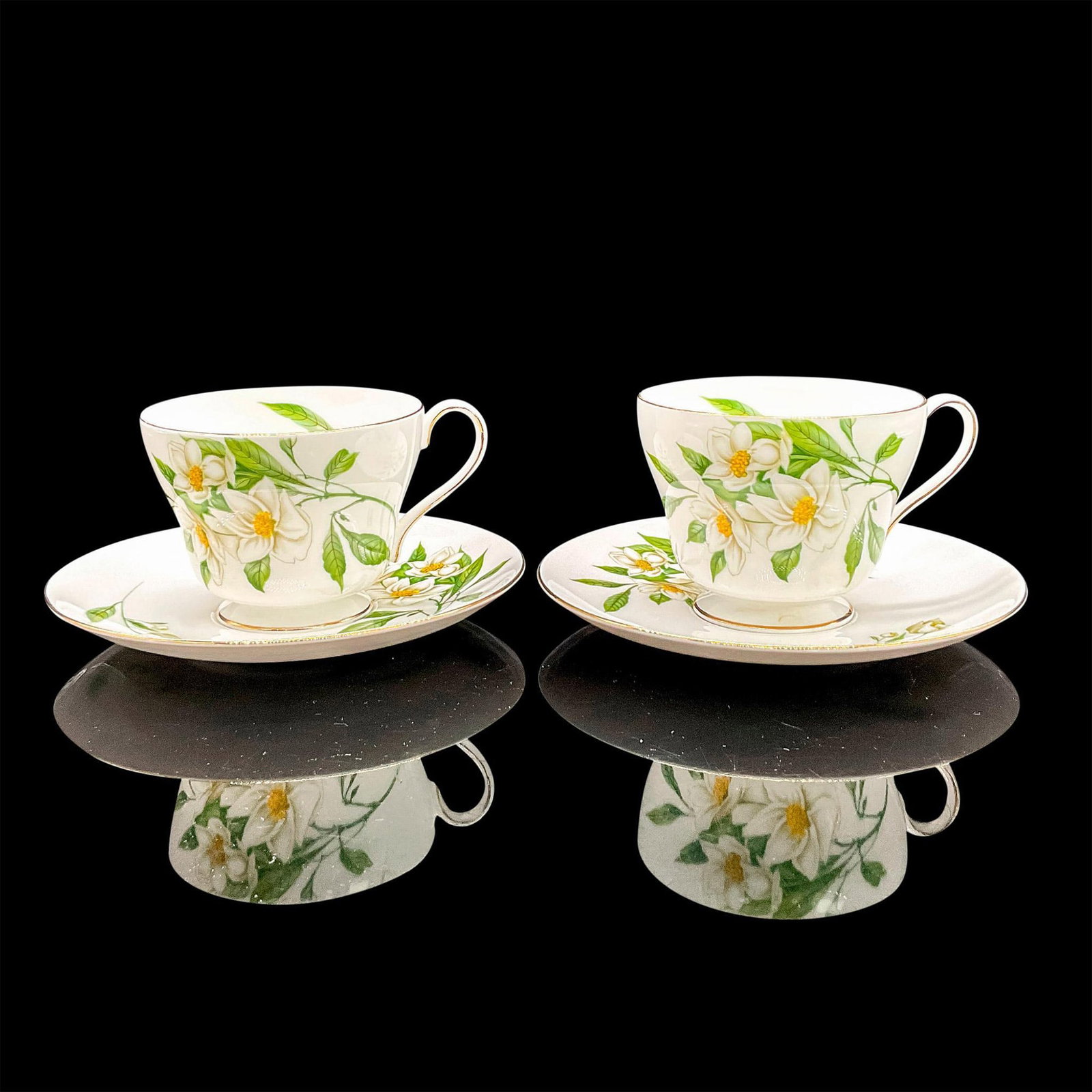 4pc Shelley England Cups and Saucers, Syringa: Vintage white bone china with white flowers and bright green leaves, gilt rims. Two tea cups and two saucers. Windsor shape. Tea cups 4"L x 3.25"W x 2.75"H. Saucers 0.75"H x 5.75"dia. Shelley England