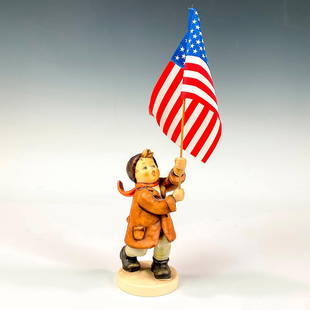 Goebel Hummel Figurine, Call To Glory: Hand painted in matte finish modeled as a boy in brown coat, cap, and burnt orange scarf holding American flag. M.I. Hummel impressed on base. Goebel backstamp Issued: 1990-1999 Dimensions: 2.5"W x 11