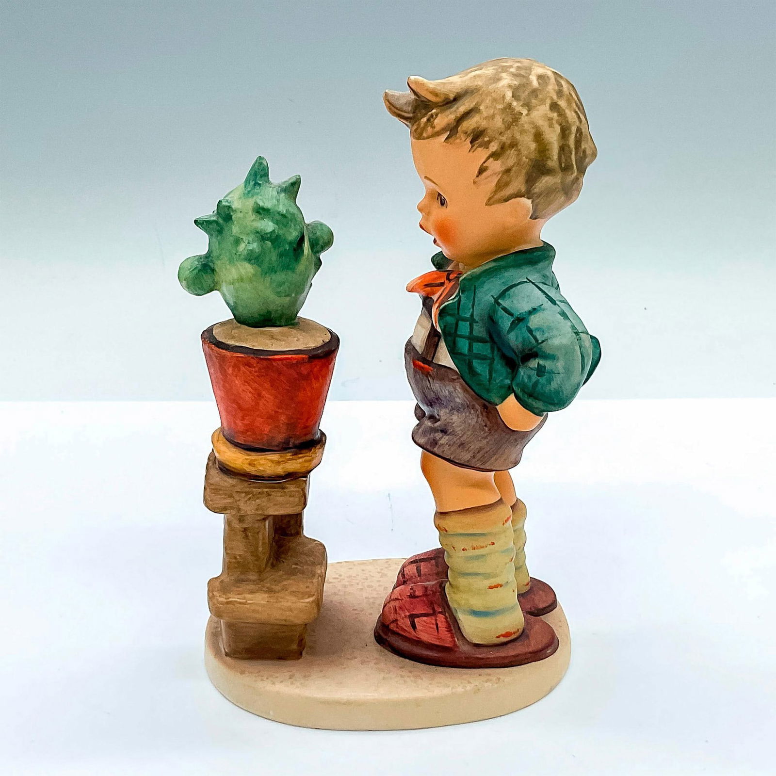 Goebel Hummel Porcelain Figurine, Confidentially HUM 314: Hand painted figure of a young boy looking at a cactus. Goebel Hummel backstamp. Issued: c. 1979-1990 Dimensions: 4"L x 2.75"W x 5.75"H Manufacturer: Goebel Hummel Country of Origin: Germany