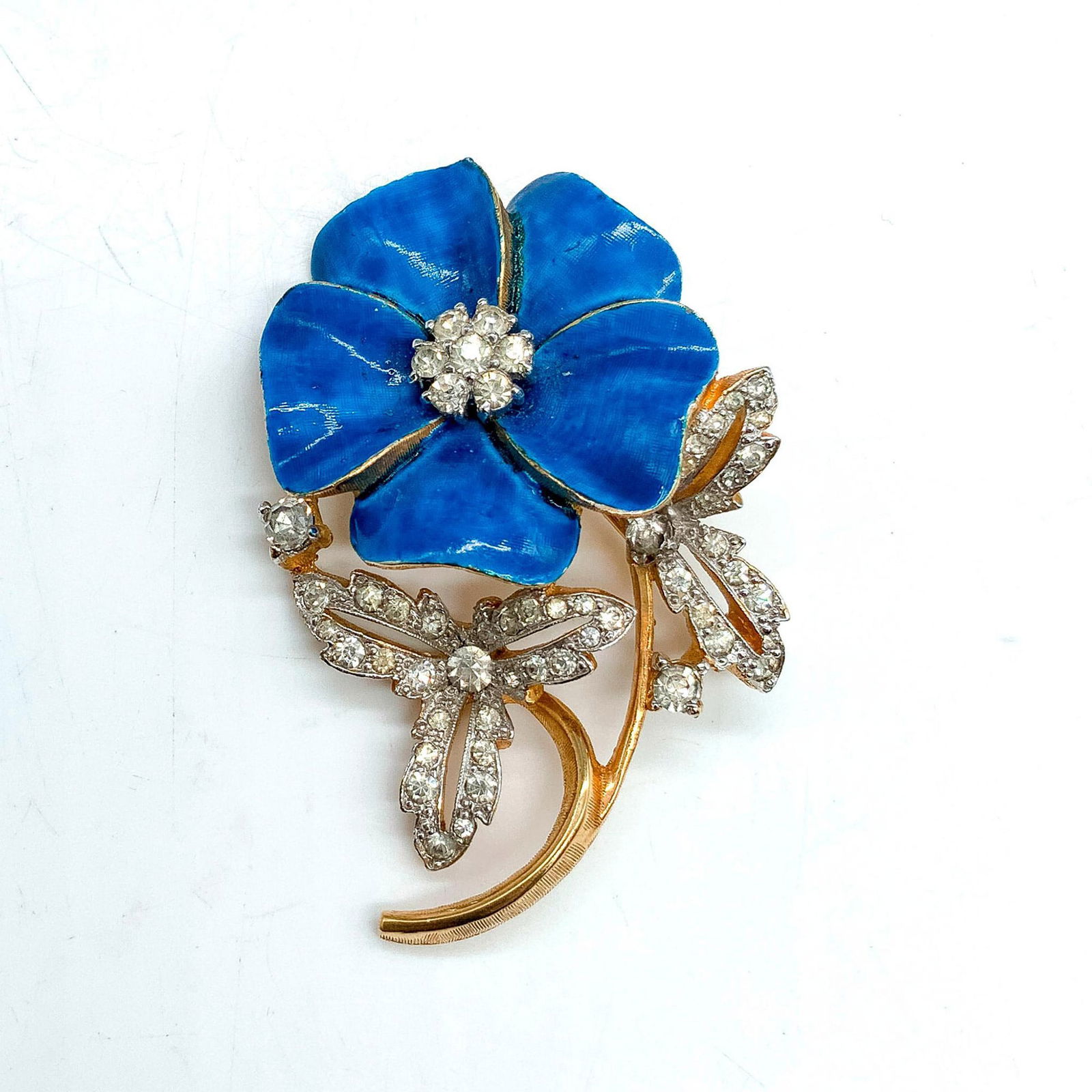 Jomaz Blue Enamel and Rhinestone Pansy Brooch Pin: Gold metal flower pin with blue enamel petals and clear rhinestone center and leaves. Dimensions: 2"L x 1.25"W Manufacturer: Jomaz Jewelry Country of Origin: United States