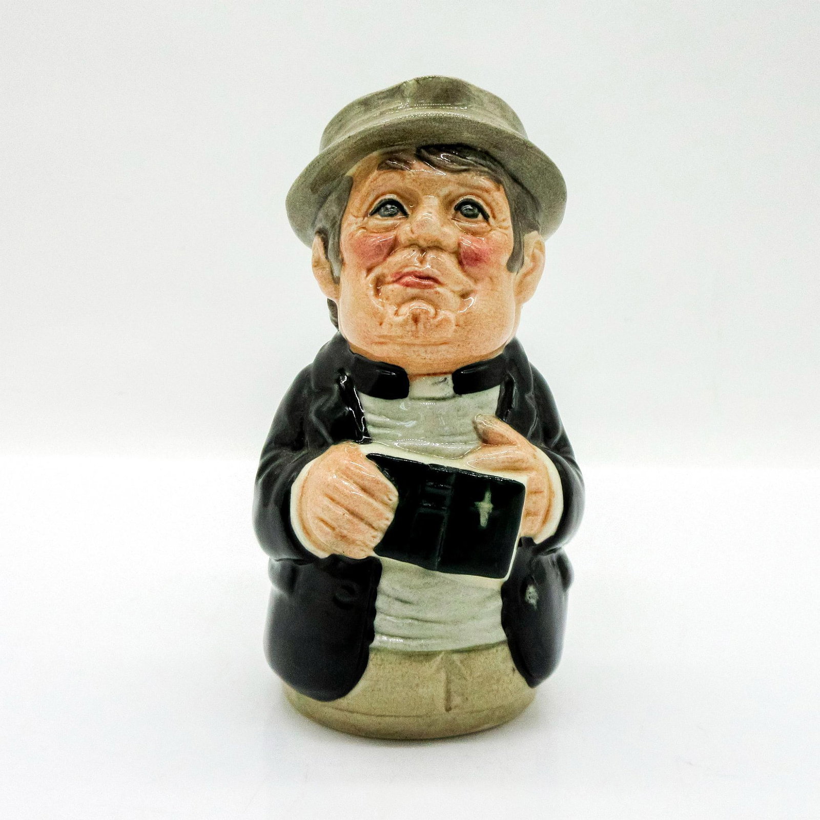 Rev. Cassock the Clergyman D6702 - Royal Doulton Toby Jug: Black coat; grey shirt; brown cap. Series: The Doultonville Collection. Royal Doulton backstamp. Artist: William K. Harper Issued: 1983 - 1990 Dimensions: 4"H Manufacturer: Royal Doulton