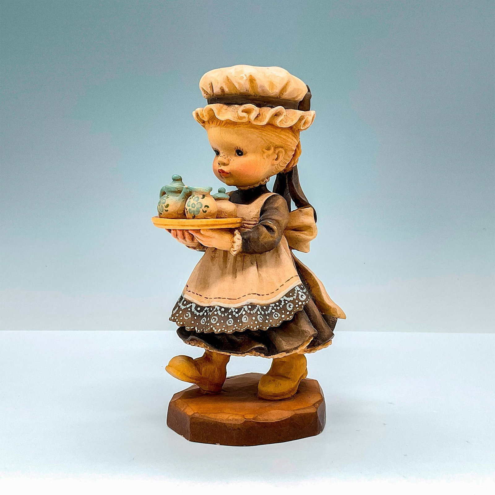 Anri Italy Wood Carved Figurine, Afternoon Tea: Delightful painted figure of a young girl in finely detailed lace apron carrying tea tray. In hues of earthy blue, brown and white. Anri metal logo emblem affixed to base. Design Valentine backstamp. 