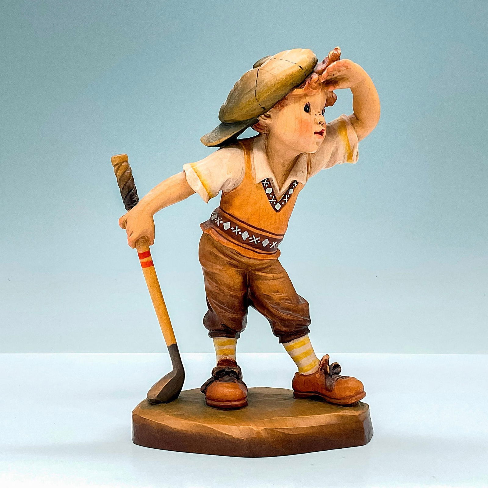Anri Italy Wood Carved Figurine, Fore: Adorable painted figure of a boy in golf attire watching ball fly. In hues of earthy orange, tan, and brown. Anri metal logo emblem affixed to base. Design John Sands backstamp. Sarah Kay engraved to