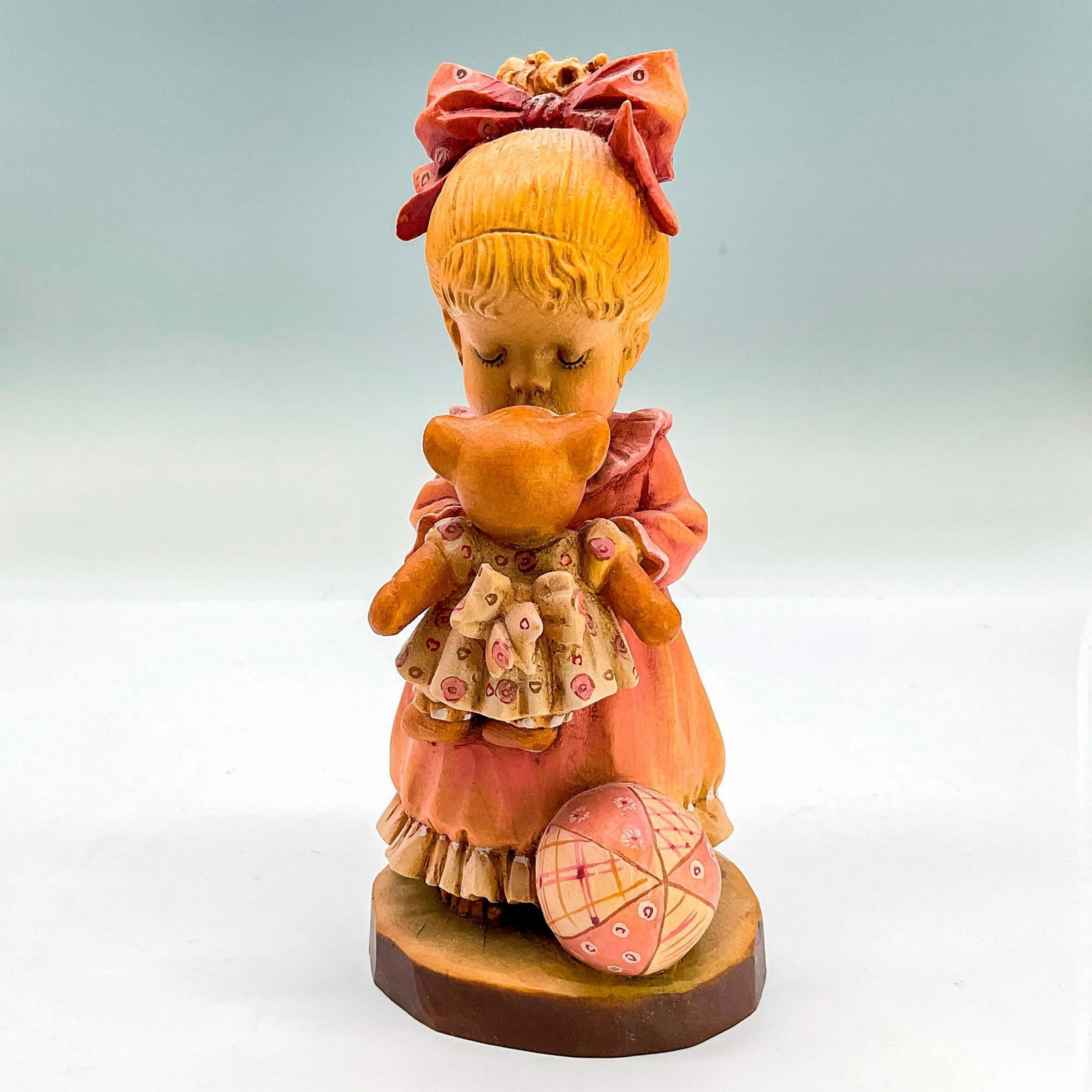 Anri Italy Wood Carved Figurine, Wake Up: Sweet painted figure of a young girl holding and kissing her teddy bear. In hues of earthy orange, pink, tan and brown. Anri metal logo emblem affixed to base. Design Valentine backstamp. Sarah Kay en