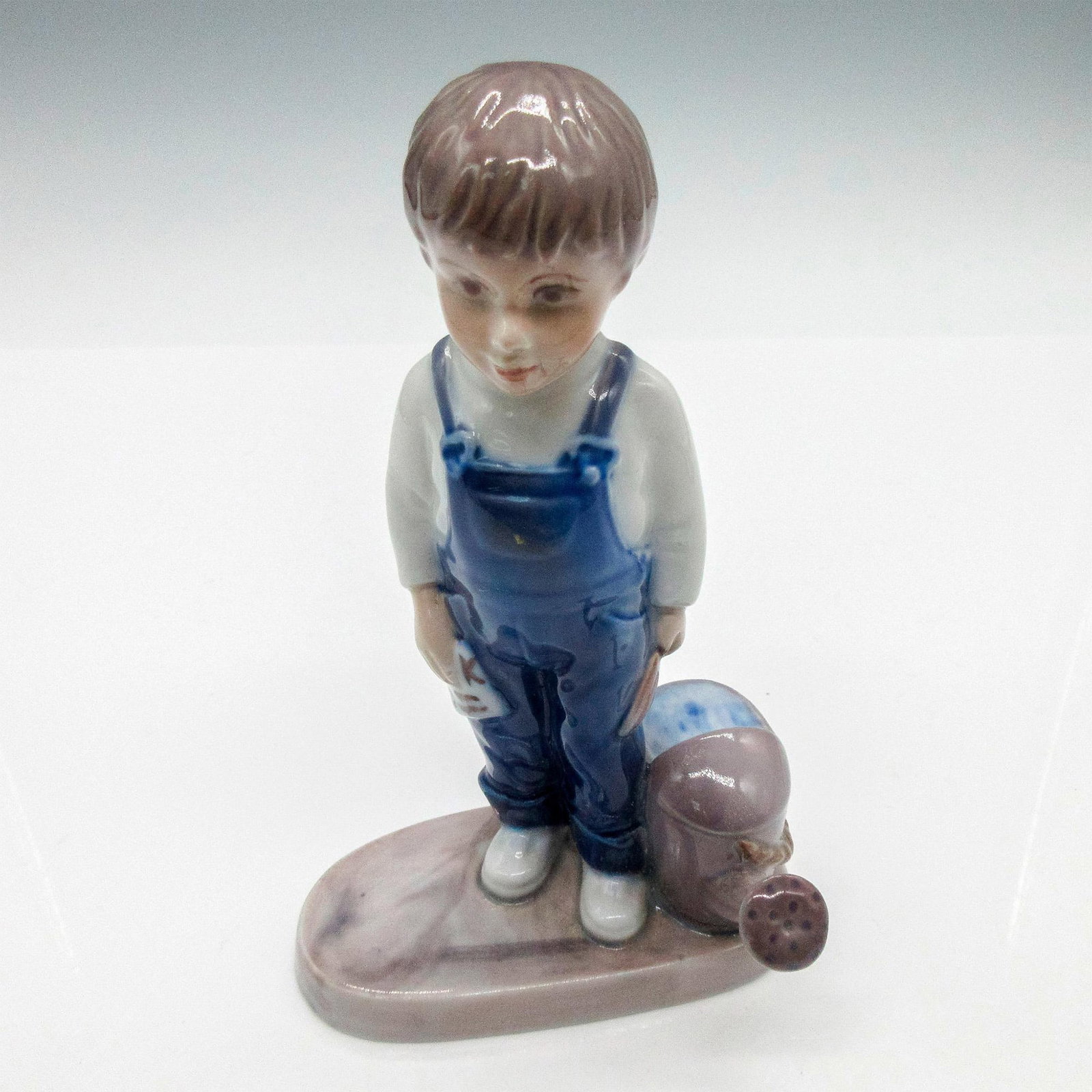 Bing & Grondahl Porcelain Figurine, Young Gardener Boy: Glossy figurine depicting an adolescent boy with a watering can by his side. Copenhagen figurine#2546. Bing & Grondahl backstamp. Dimensions: 4"L x 3"W x 6.50"H Issued: 20th century Edition Number: 25