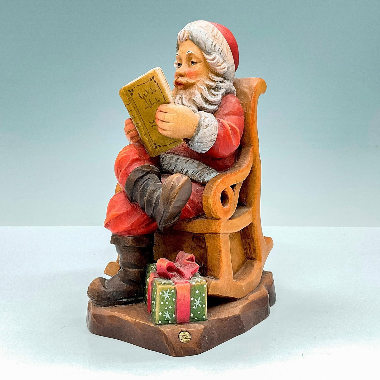 Anri Italy Wood Carved Figurine, Mr. Santa Signed: Magical painted figure of Santa in his rocking chair. In hues of earthy red, green, and brown. Anri metal logo affixed to base. Sarah Kay engraved to back of base. Signed by artist. Dimensions: 4.75"L
