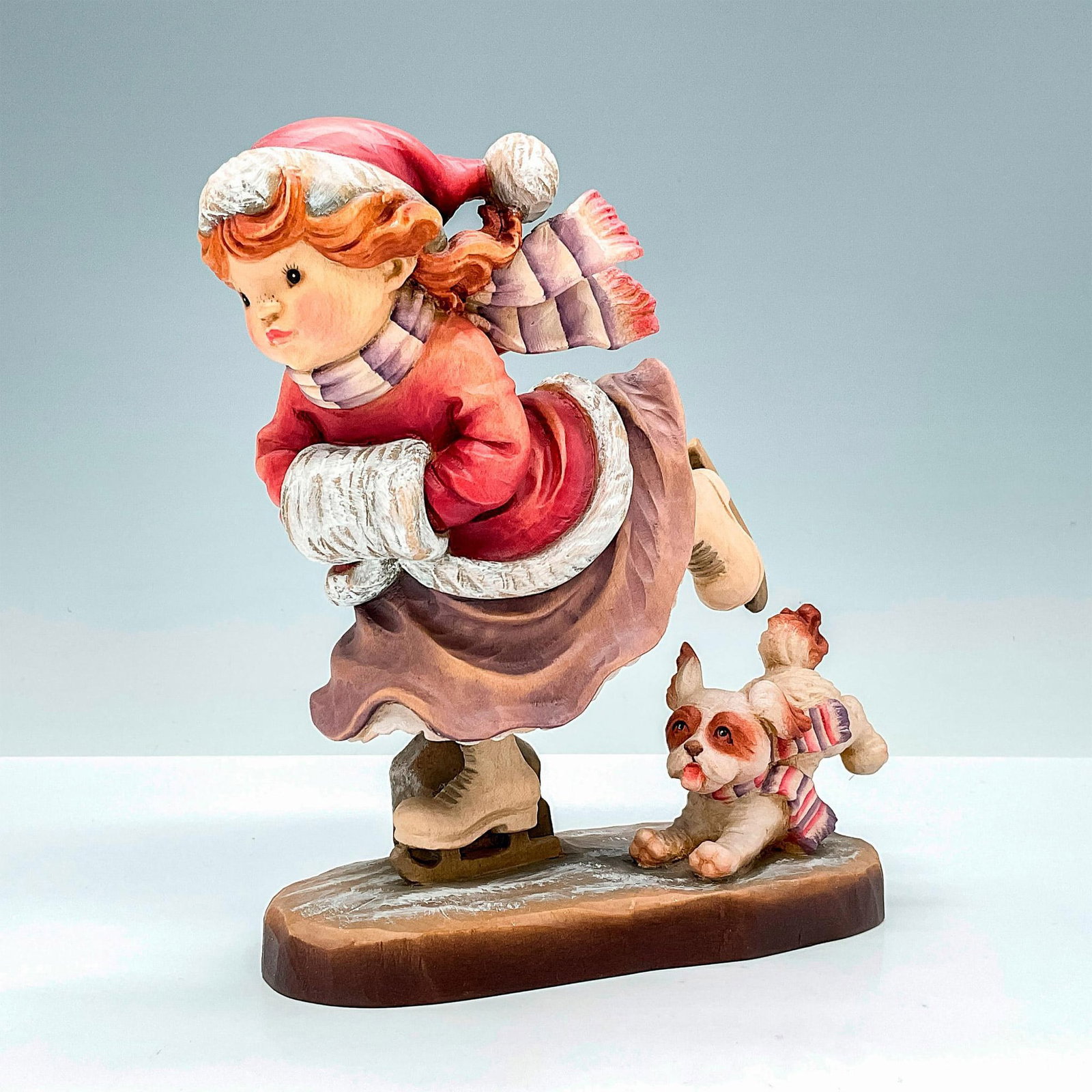 Anri Italy Wood Carved Figurine, Figure Eight: Captivating painted figure of a young girl ice skating with her dog. In hues of earthy red, orange, tan and brown. Anri metal logo emblem affixed to base. Design Valentine backstamp. Sarah Kay engrave