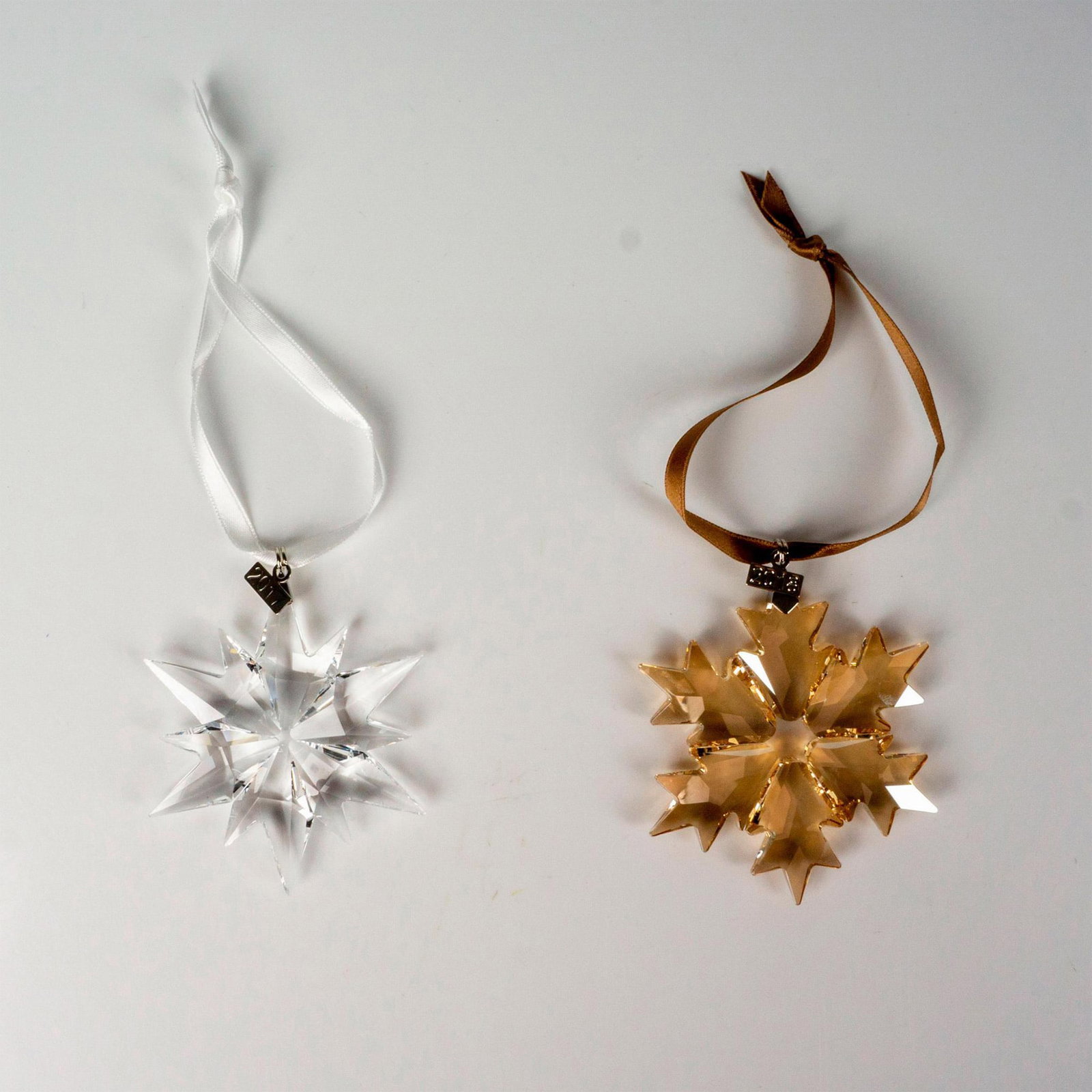 2pc Swarovski Crystal Christmas Ornaments: Lead clear and golden shadow colored crystals part of the Christmas Ornaments collection. They hang with a brown and white satin ribbon. Swarovski etched backstamp. This item has its original box. Box
