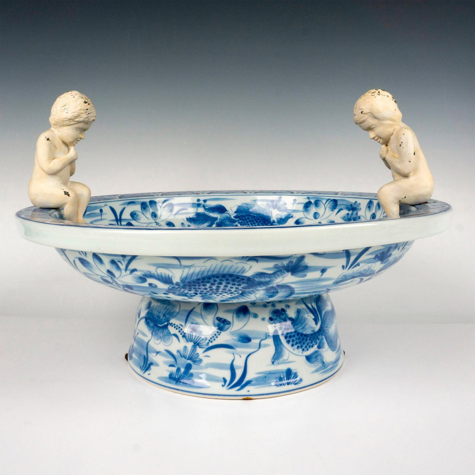 Maitland Smith Chinoiserie Blue & White Centerpiece: Beautiful blue and white porcelain footed bowl with two seated putti. The bowl is hand decorated in the Chinese style with koi and lily pads. Maitland Smith sticker on the underside. Dimensions: 16.75