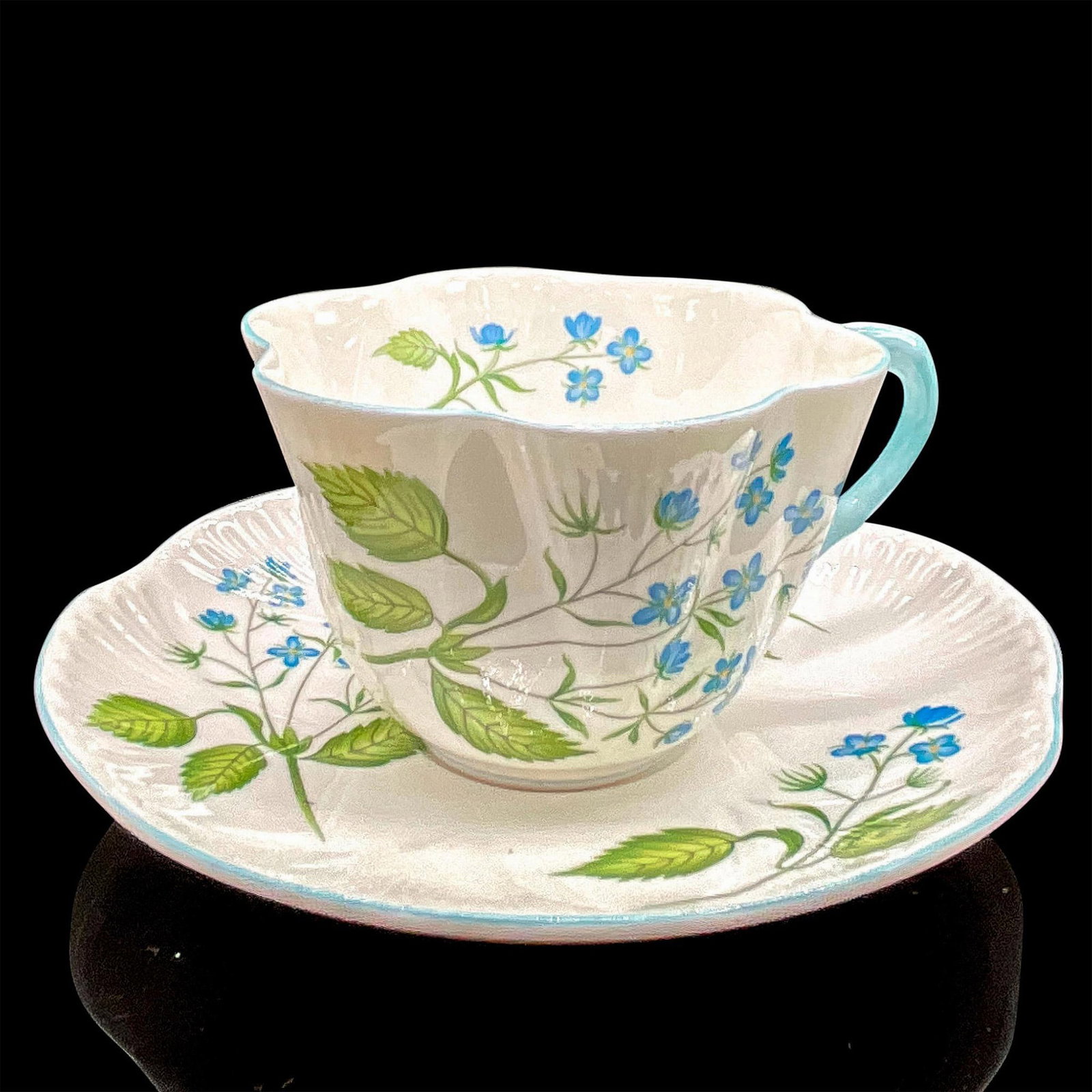 2pc Shelley England Cup and Saucer, American Brooklime: White bone china with delicate blue flowers, blue rims. Dainty shape. Tea cup 4"L x 3.5"W x 2.5"H. Saucer 0.75"H x 5.5"dia. Shelley England backstamp. Manufacturer: Shelley Country of Origin: England