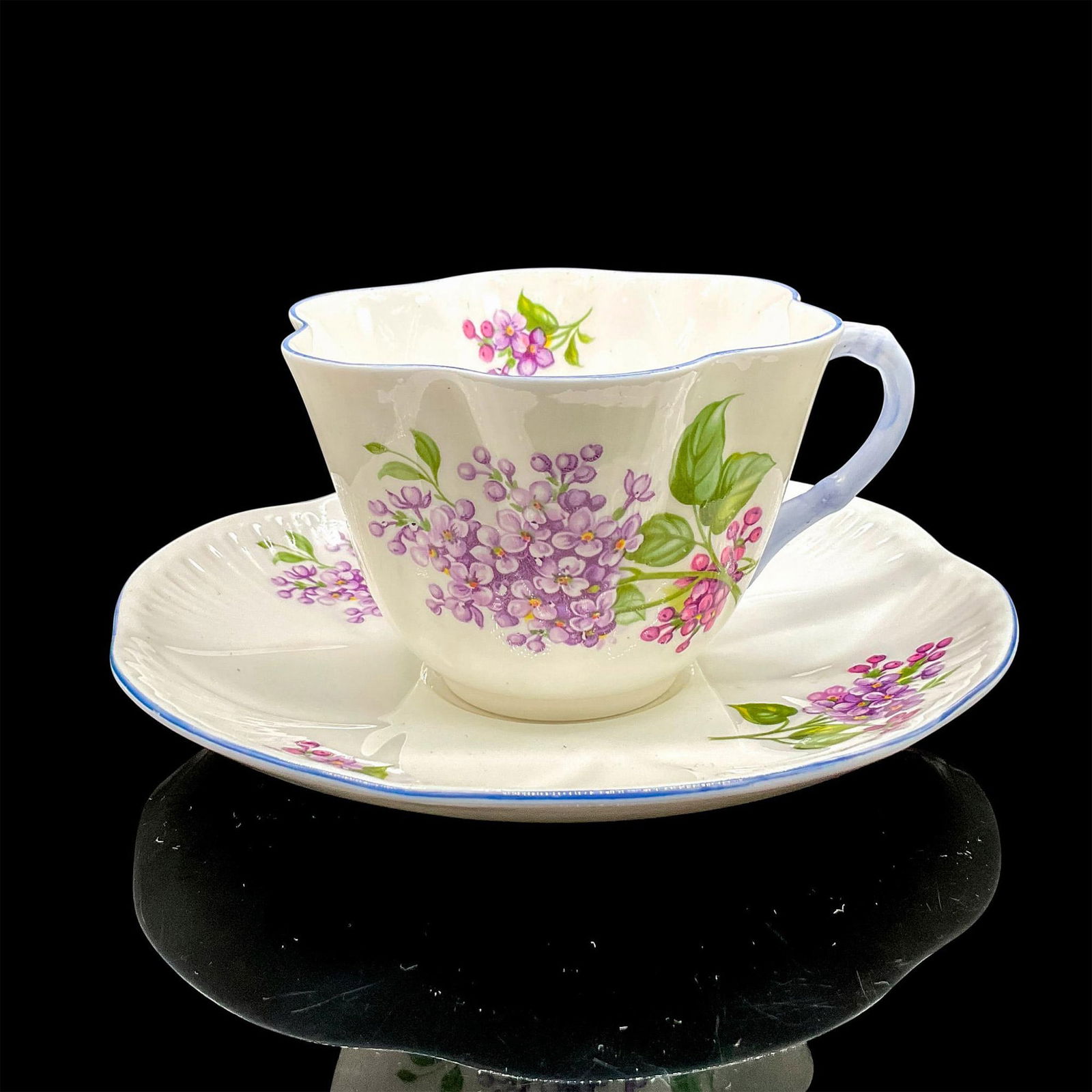 2pc Shelley England Cup and Saucer, Lilac Time: White bone china with delicate purple flowers, violet blue rim. Dainty shape. Tea cup 4"L x 3.5"W x 2.5"H. Saucer 0.75"H x 5.75"dia. Shelley England backstamp. Manufacturer: Shelley Country of Origin:
