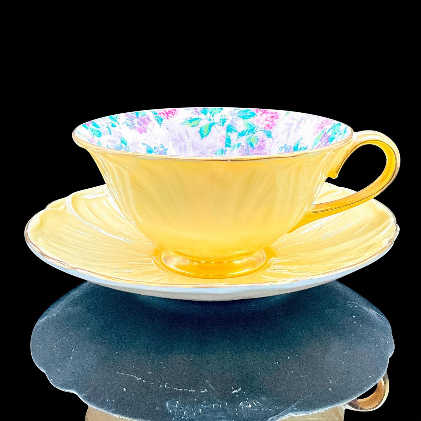 2pc Shelley England Cup and Saucer, Summer Glory Hydrangea: Bone china in a yellow glaze. Interior is pale pink with delicate purple, blue, white and pink flowers, gilt rim. Oleander shape. Tea cup 5"L x 4"W x 2"H. Saucer 1"H x 5.75"dia. Shelley England backst