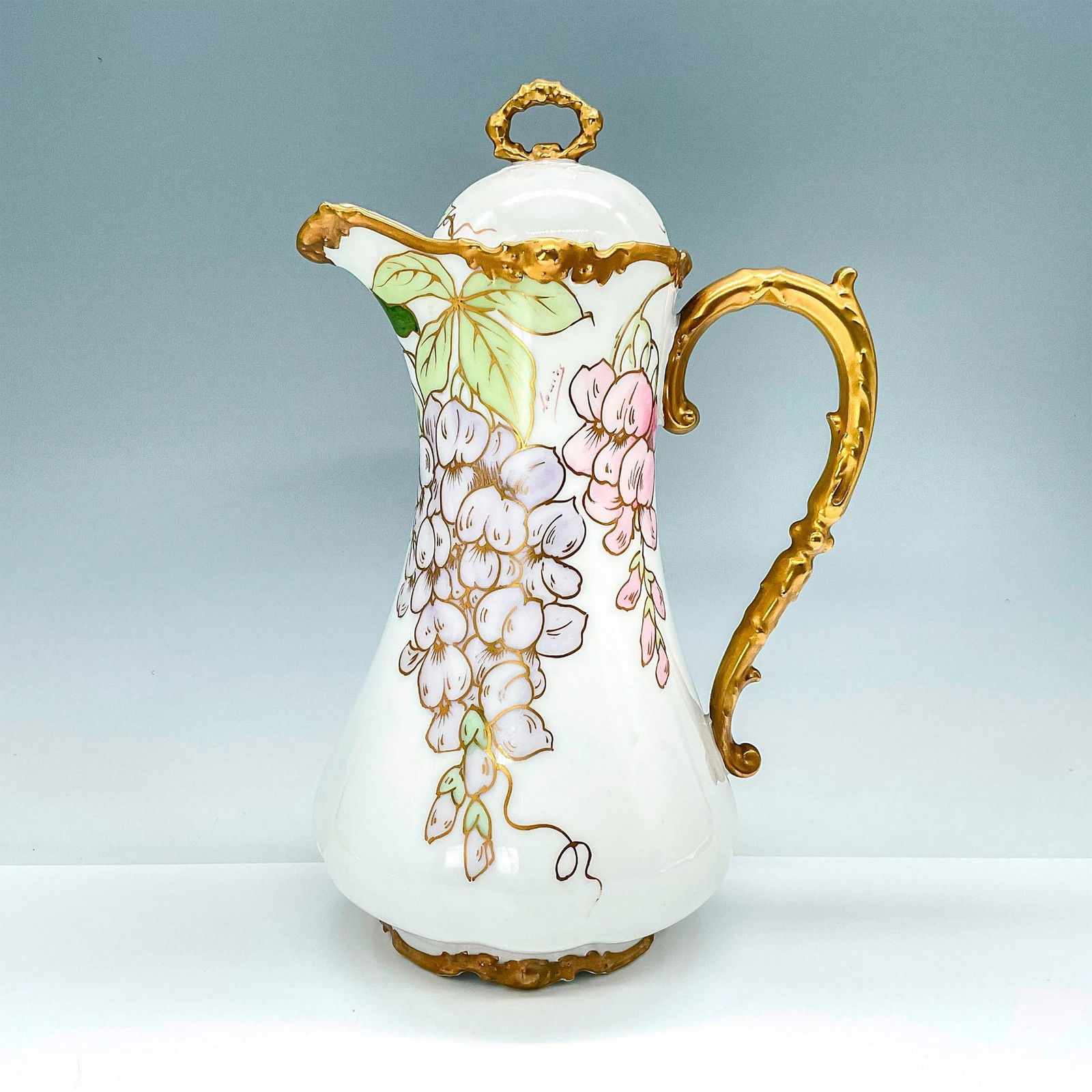 La Seynie Limoges Porcelain Lidded Pitcher, Gold w/Flowers: Elegant bone white lidded pitcher, highly gilded and decorated with hand painted pink and purple flowers. La Seynie Limoges backstamp. Signed Louis to the outside. Dimensions: 7"L x 5.5"W x 10.75"H Co