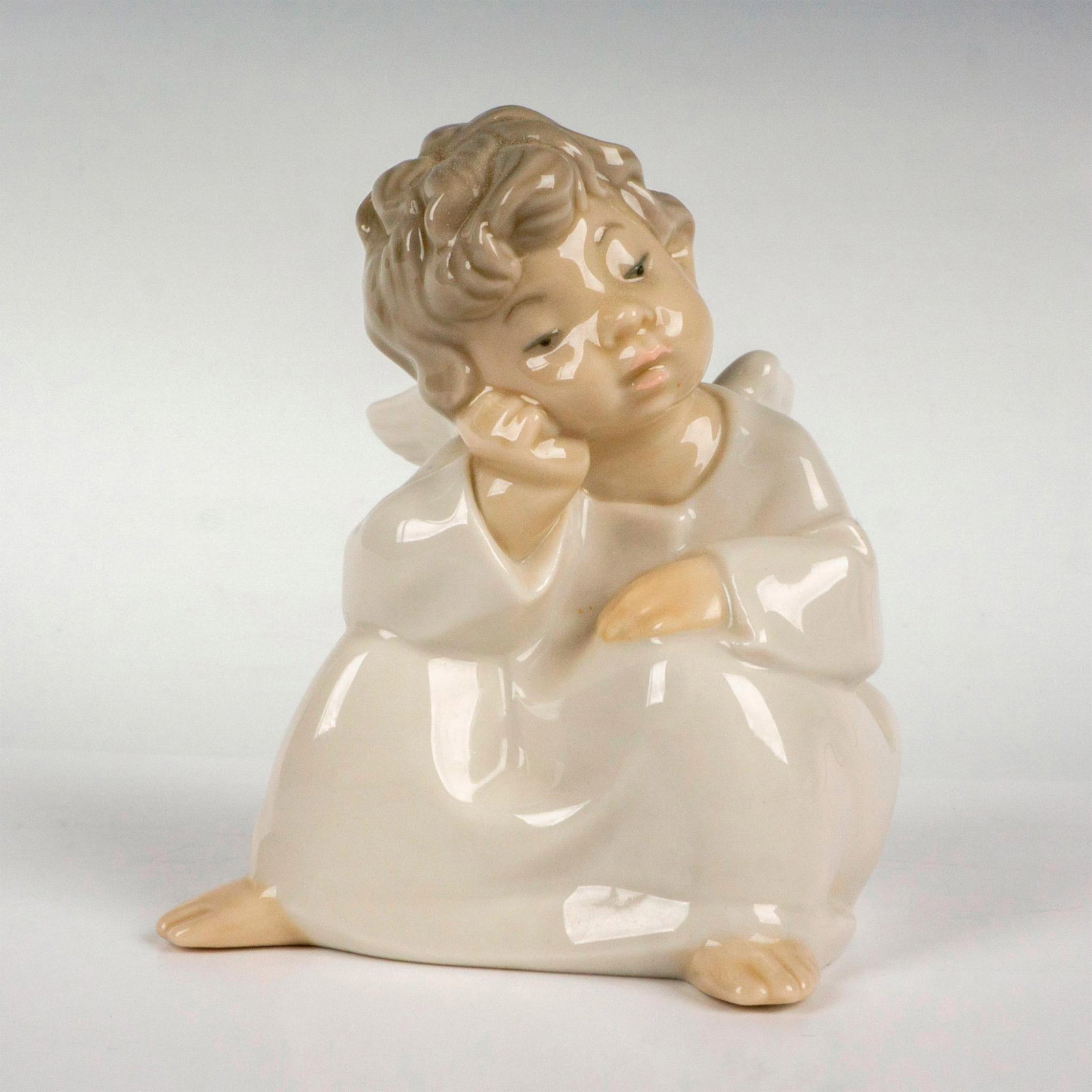Angel Thinking 1004539 - Lladro Porcelain Figurine: Glossy finish; Lladro backstamp. Artist: Fulgencio Garcia Issued: 1969 Dimensions: 4"H x 4"W Manufacturer: Lladro Country of Origin: Spain