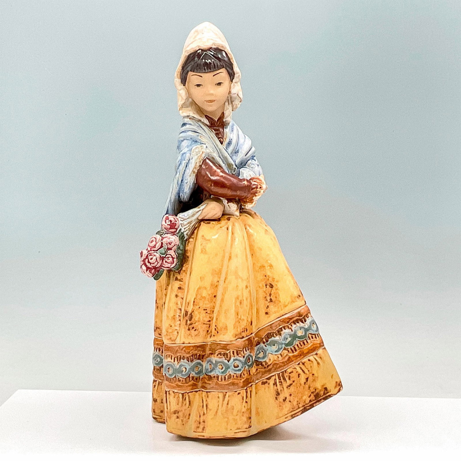 Fiesta 1013505 - Lladro Porcelain Figurine: Charming figurine of a woman in headscarf and shawl hold a bouquet of roses. Gres finish. Lladro backstamp. Artist: Salvador Debon Issued: 1978-1988 Dimensions: 7"L x 7"W x 14"H Manufacturer: Lladro